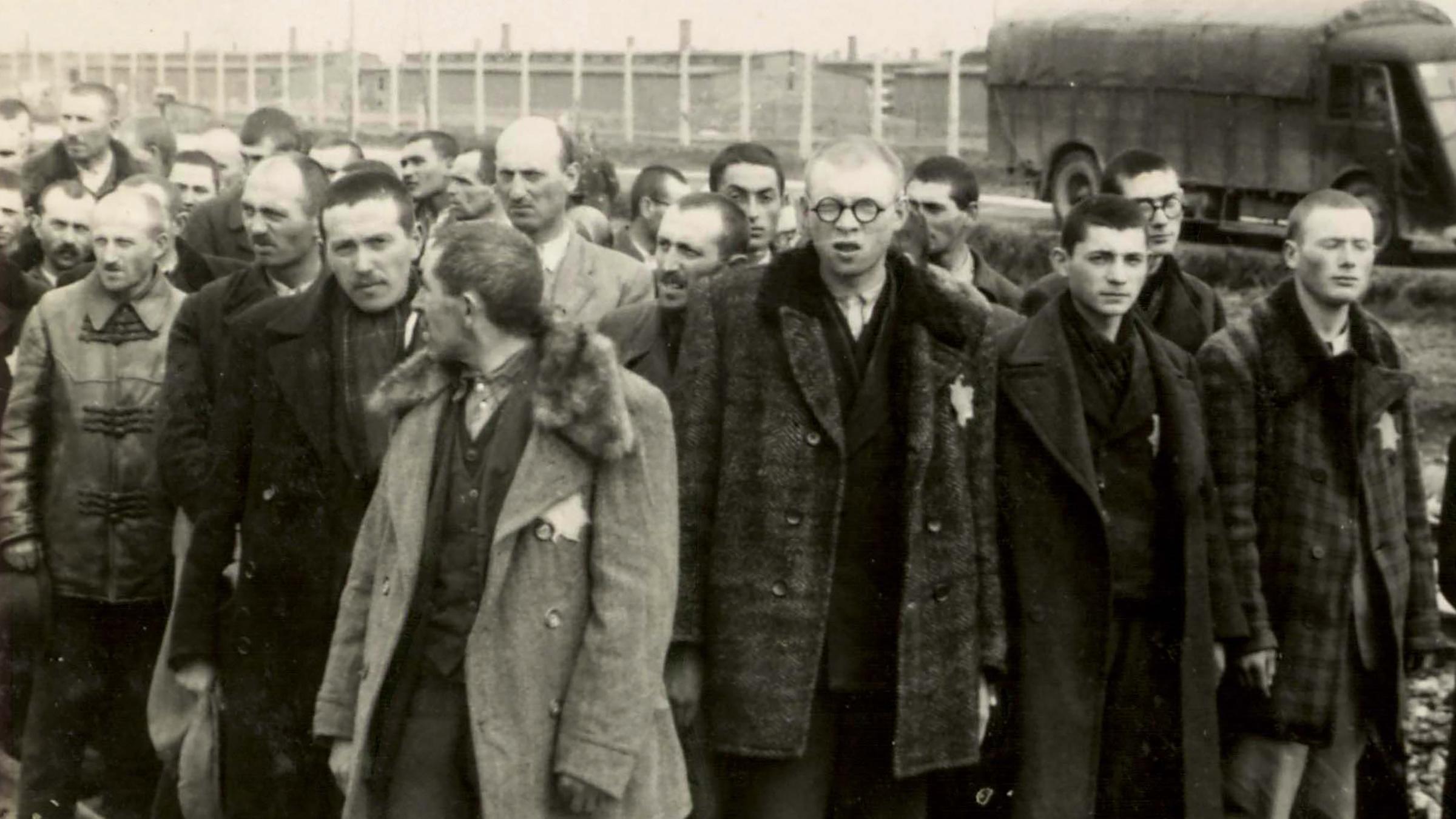 KZ Auschwitz-Birkenau - Nur die jungen Männer aus dem Bild zuvor stehen jetzt im „Wartebereich“ auf den Gleisen.  Alle alten Männer sind verschwunden. 