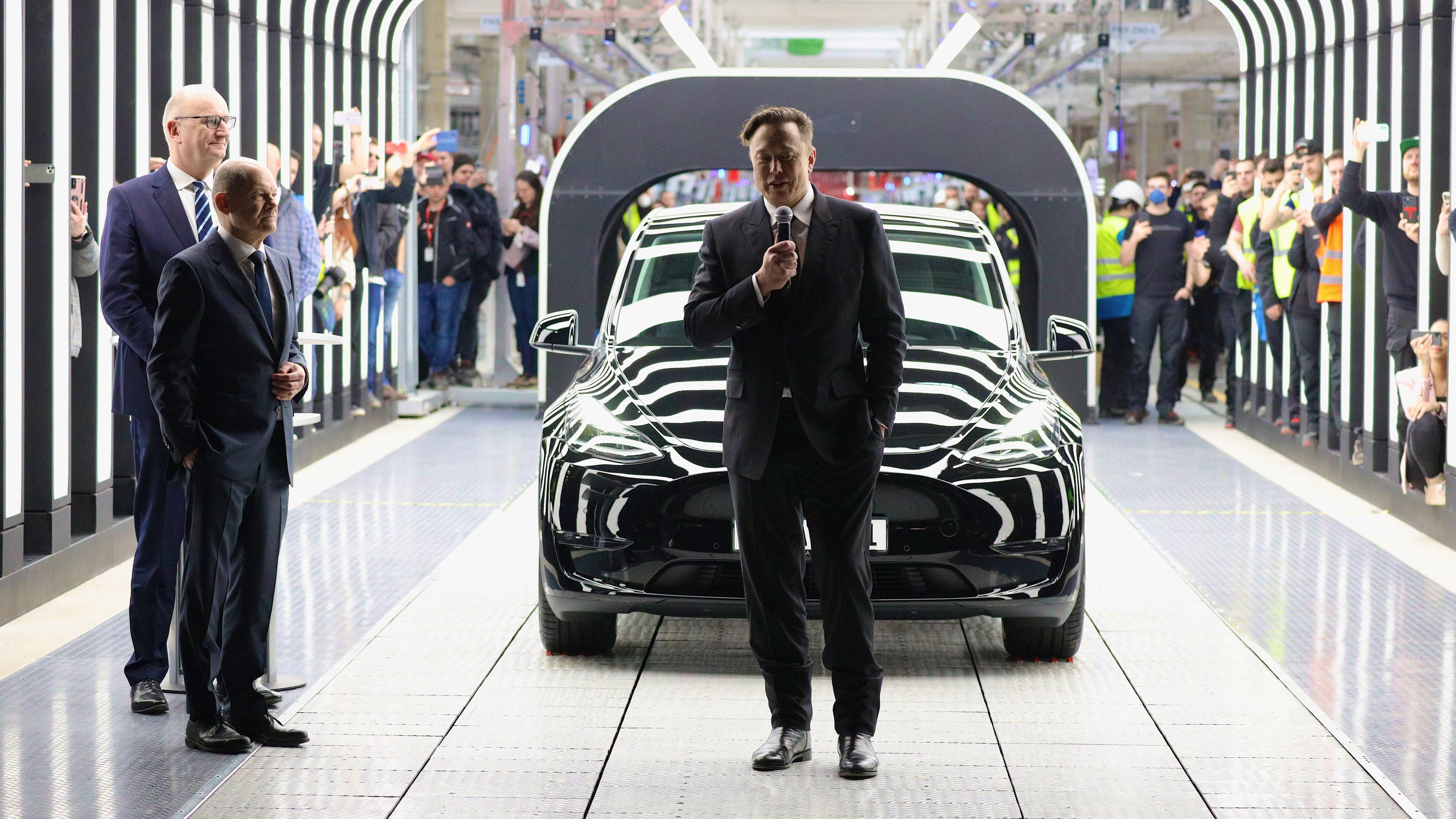 Grünheide bei Berlin, Deutschland, 22.03.2022: Tesla CEO Elon Musk spricht während der Eröffnung der Tesla "Gigafactory" vor einem Tesla auf einem großen Rollband. Bundeskanzler Scholz steht daneben