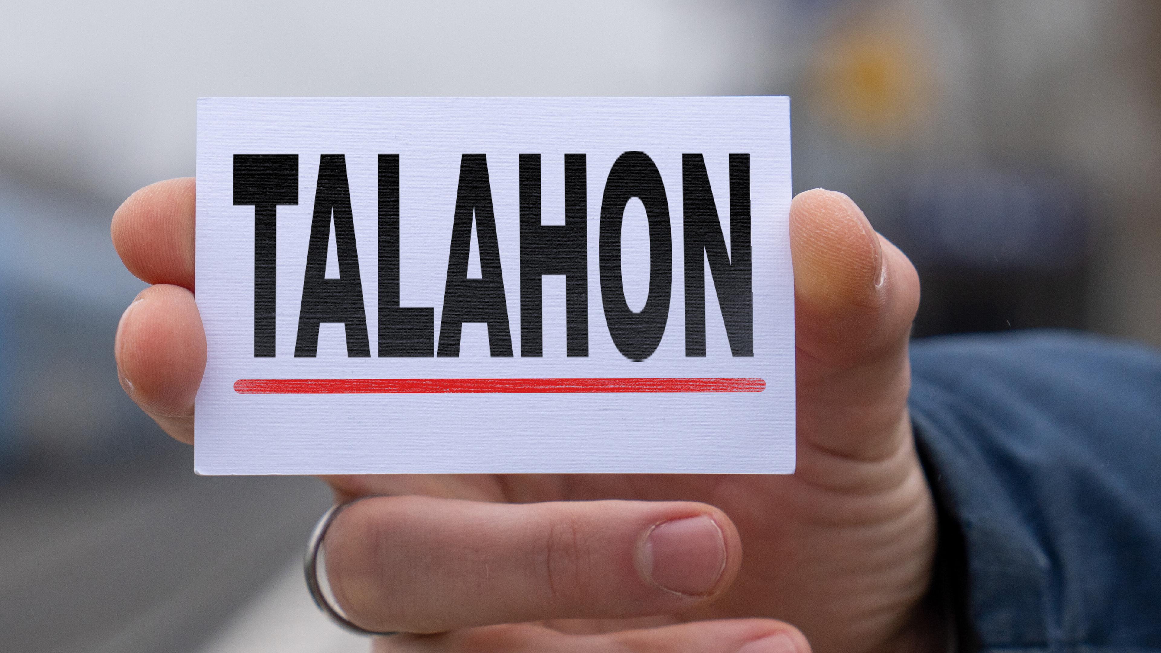 A person holds a sign with the text Talahon up to the camera.A person holds a sign with the text Talahon up to the camera.