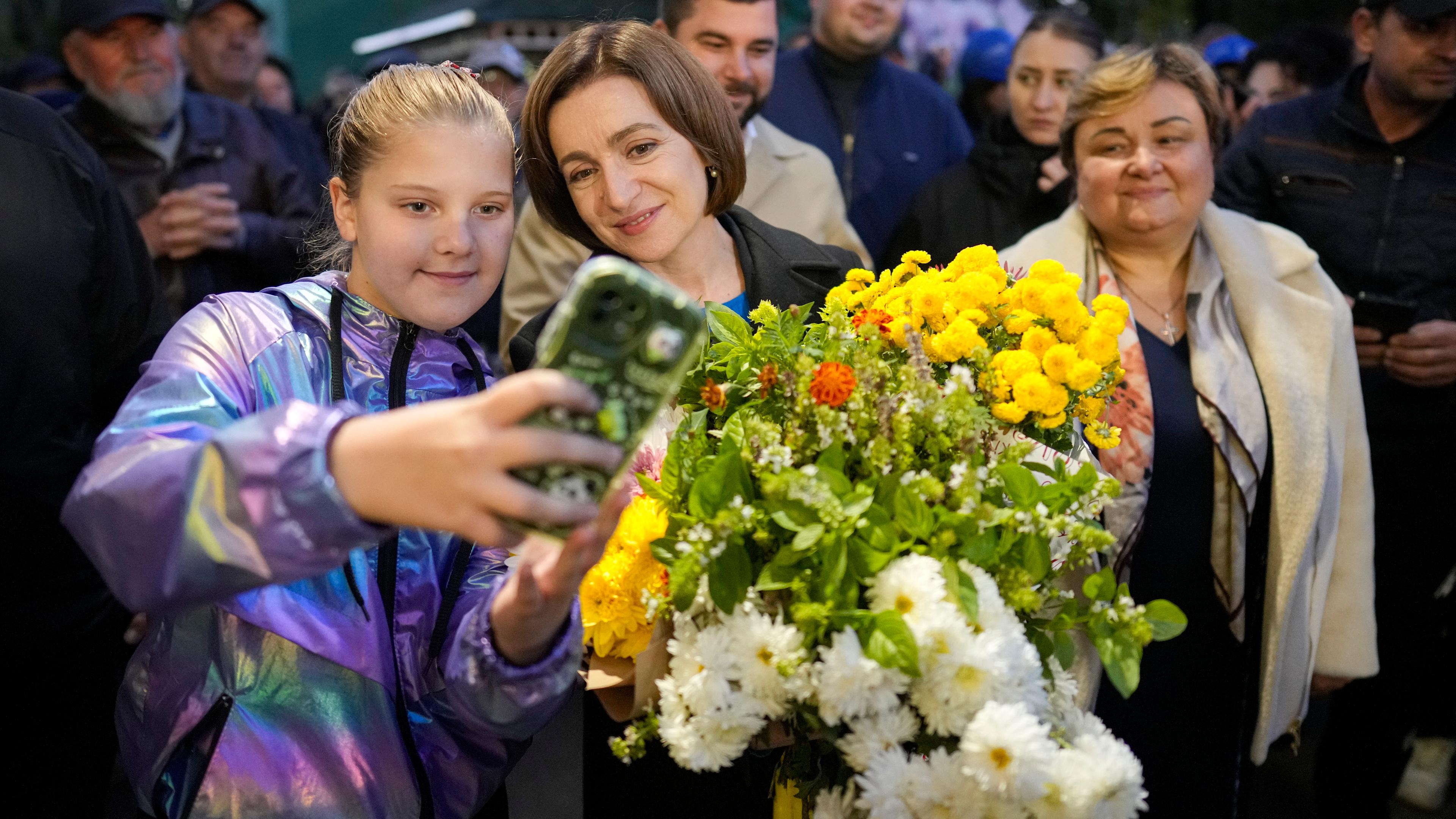 Maia Sandu (M), Präsidentin von Moldau, posiert für ein Selfie, während sie bei einer Wahlversammlung Blumensträuße hält. Bei den Wahlen am 20. Oktober strebt sie eine zweite Amtszeit an. Außerdem stimmt das Land an diesem Tag darüber ab, ob der Weg zur Mitgliedschaft in der Europäischen Union in der Verfassung Moldaus verankert werden soll.