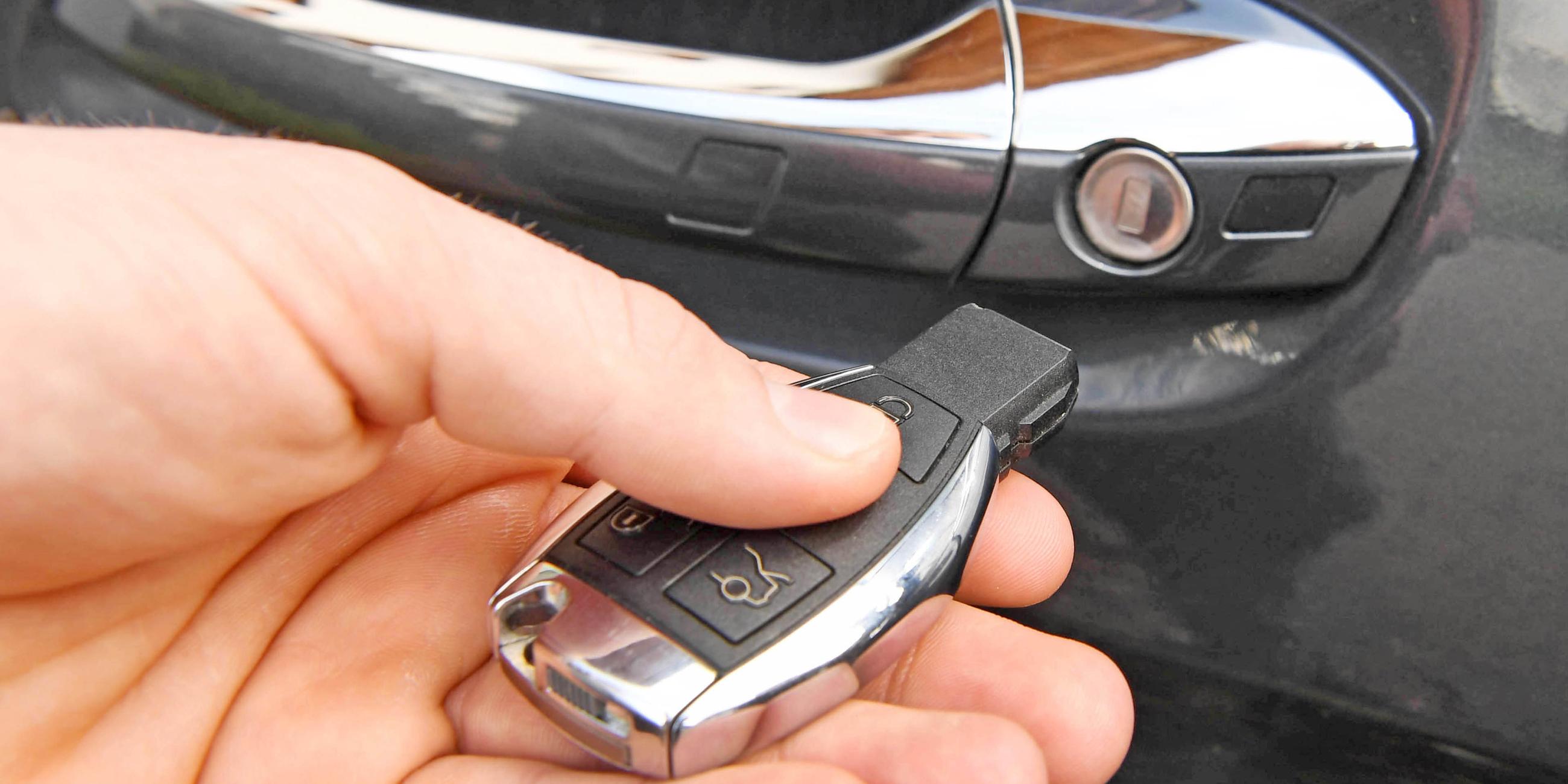 Hand mit Autoschlüssel, im Hintergrund ein Autotürgriff