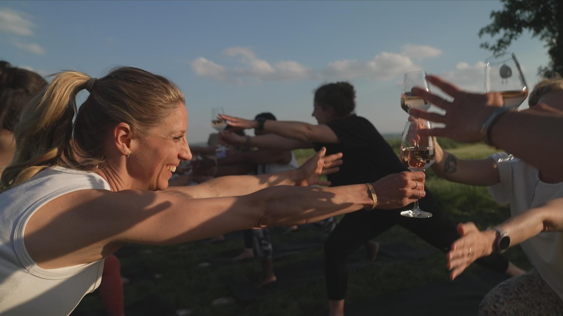 Eine Gruppe Frauen macht Yoga-Posen mit Weingläsern in der Hand und lacht