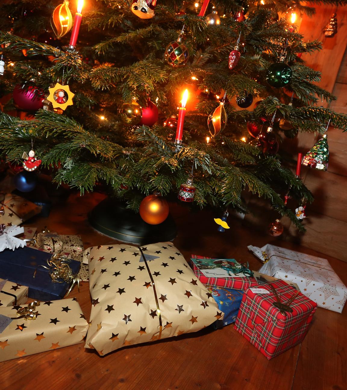 Unter einem weihnachtlich beschmücktem Tannenbaum liegen viele in gold und rote verpackte Geschenke