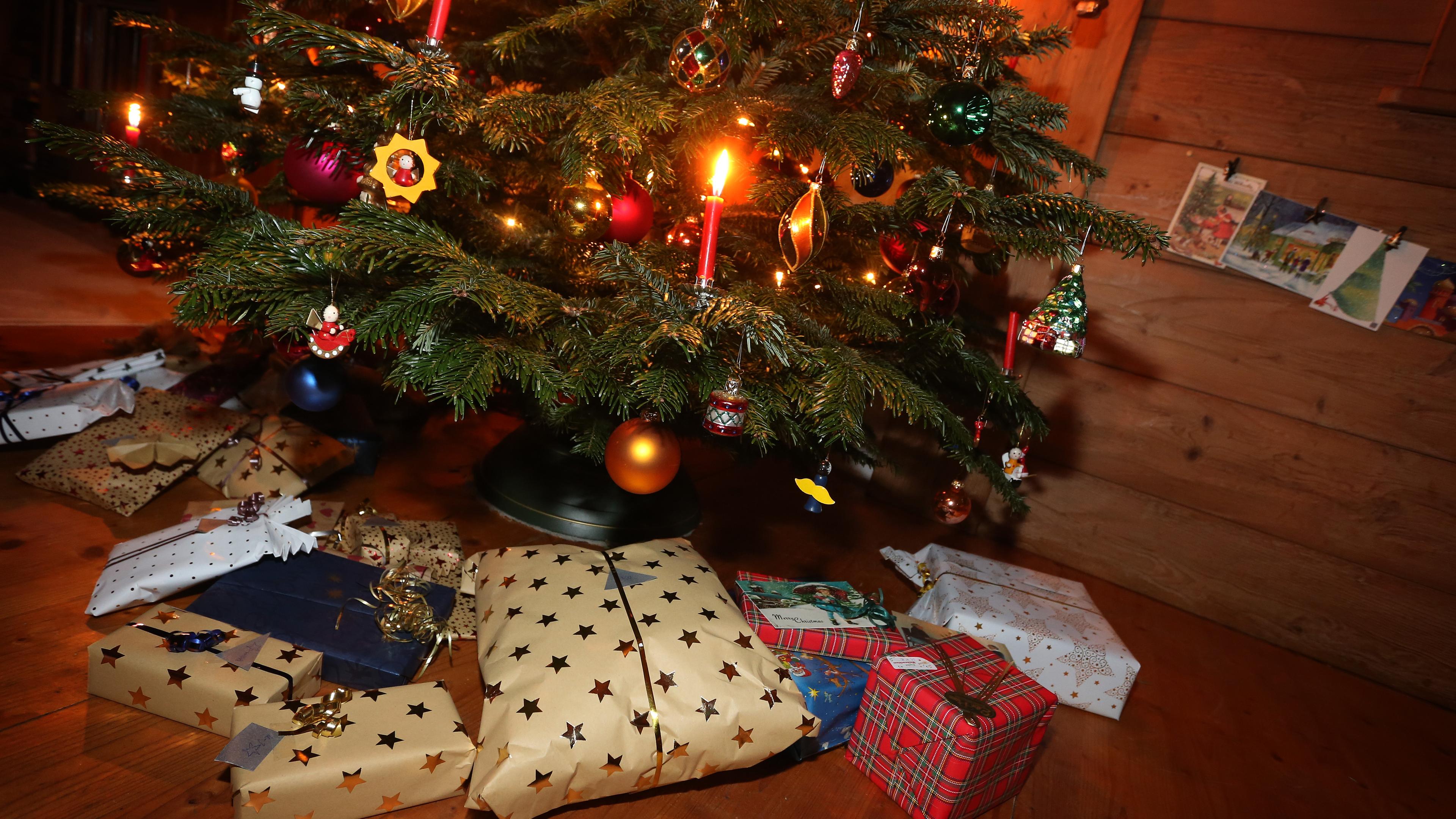 Unter einem weihnachtlich beschmücktem Tannenbaum liegen viele in gold und rote verpackte Geschenke