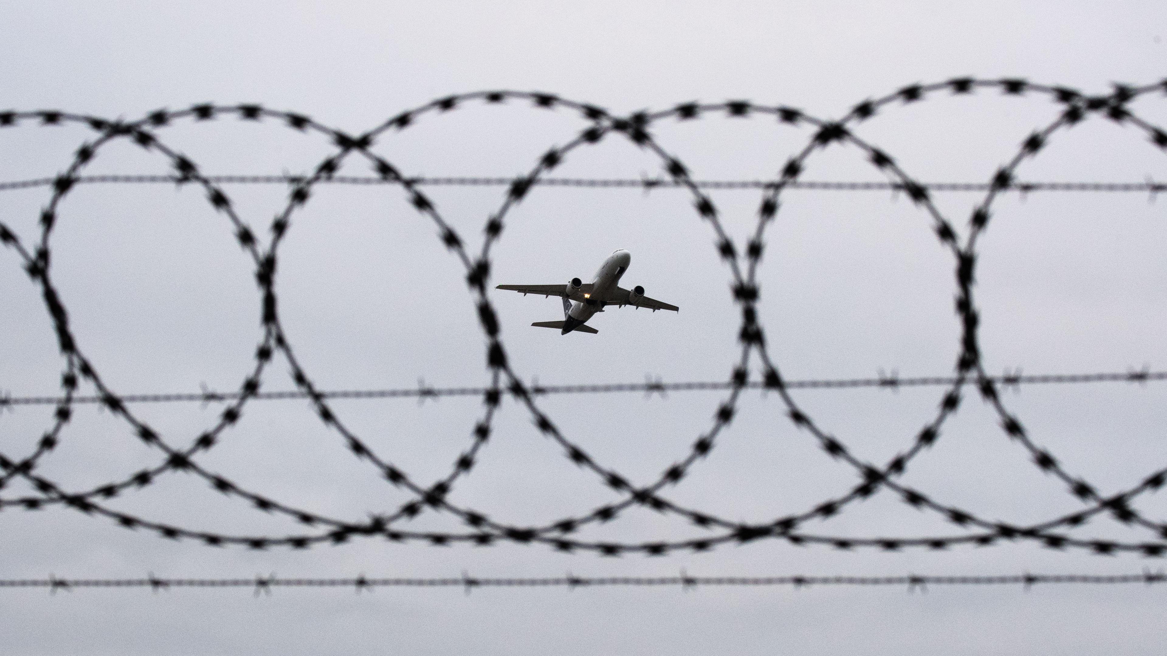 Symbolbild: Ein Flugzeug startet am Flughafen Hannover - fotografiert durch Stacheldraht am Flughafenzaun. 