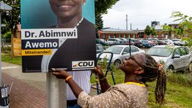 Adeline Abimnwi Awemo steht neben einem Wahlplakat der CDU, auf dem sie abgebildet ist.