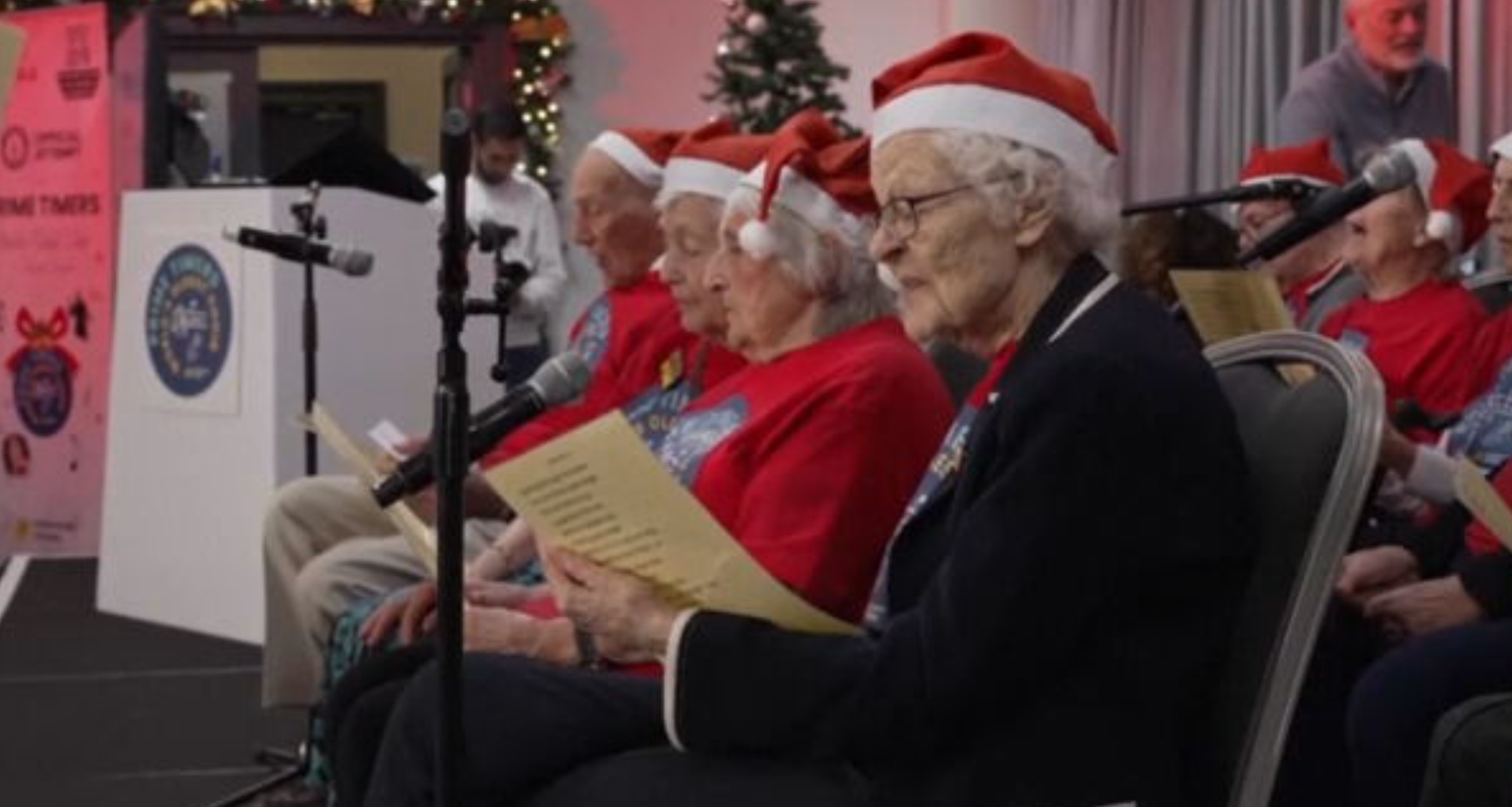 Alte Menschen sitzen mit Weihnachtsmützen auf dem Kopf zusammen und singen Weihnachtslieder.