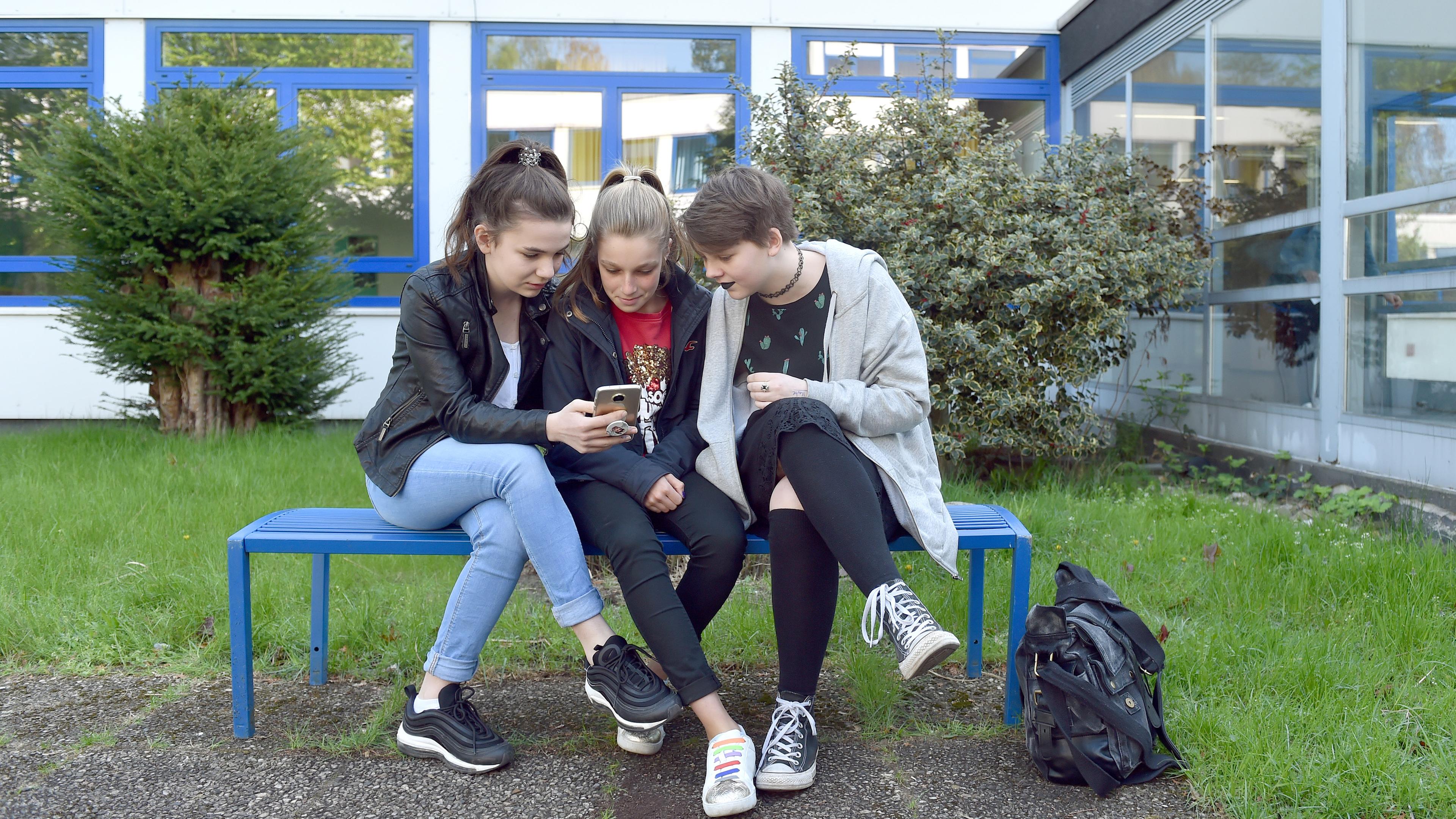 maedchen sitzen mit smartphone auf schulhof