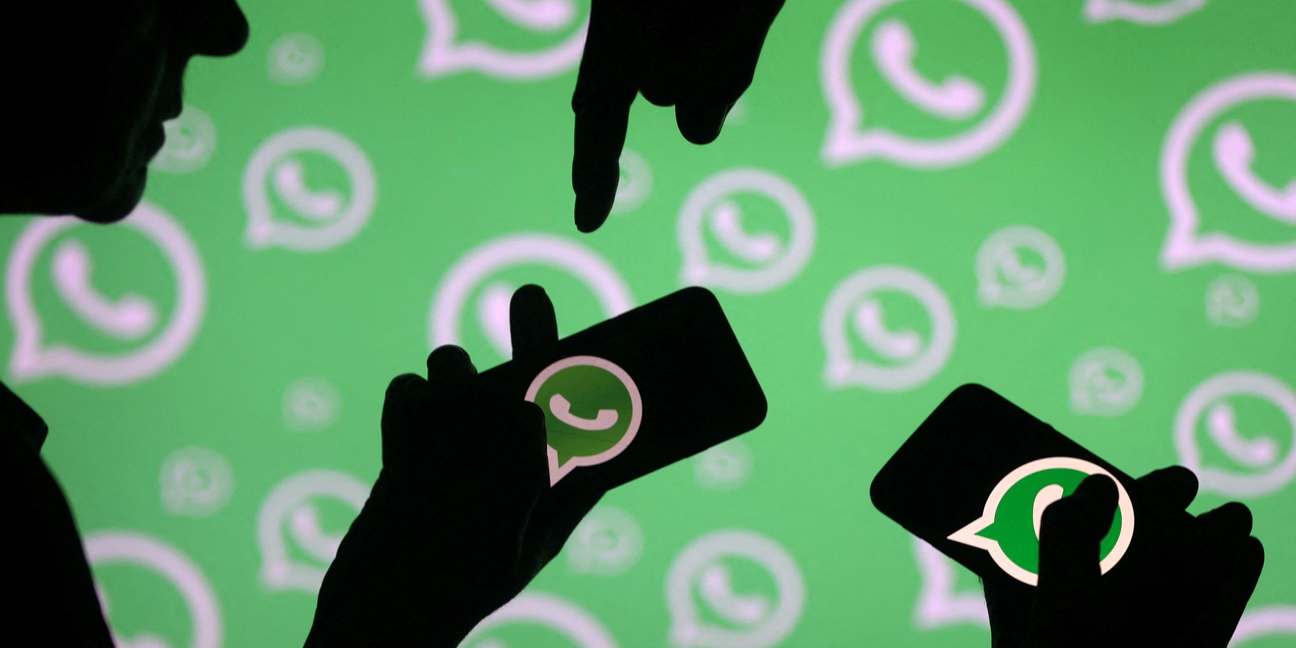 FILE PHOTO: Men pose with smartphones in front of displayed Whatsapp logo