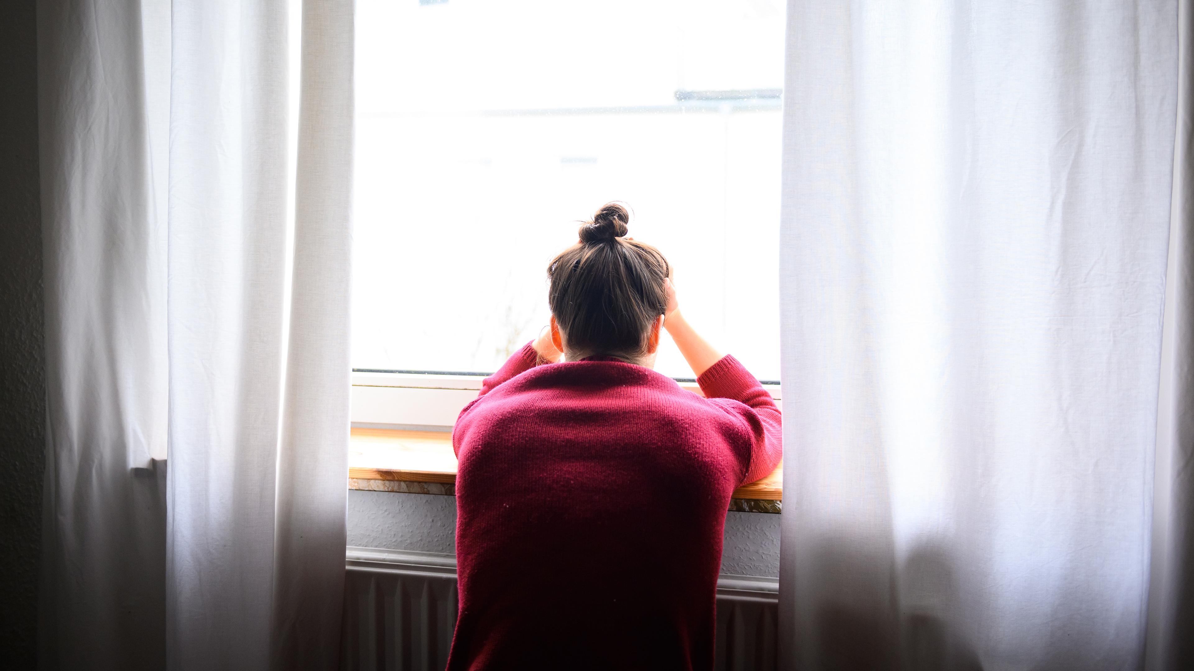 Das Bild zeigt eine Frau, die verzweifelt aus dem Fenster schaut.