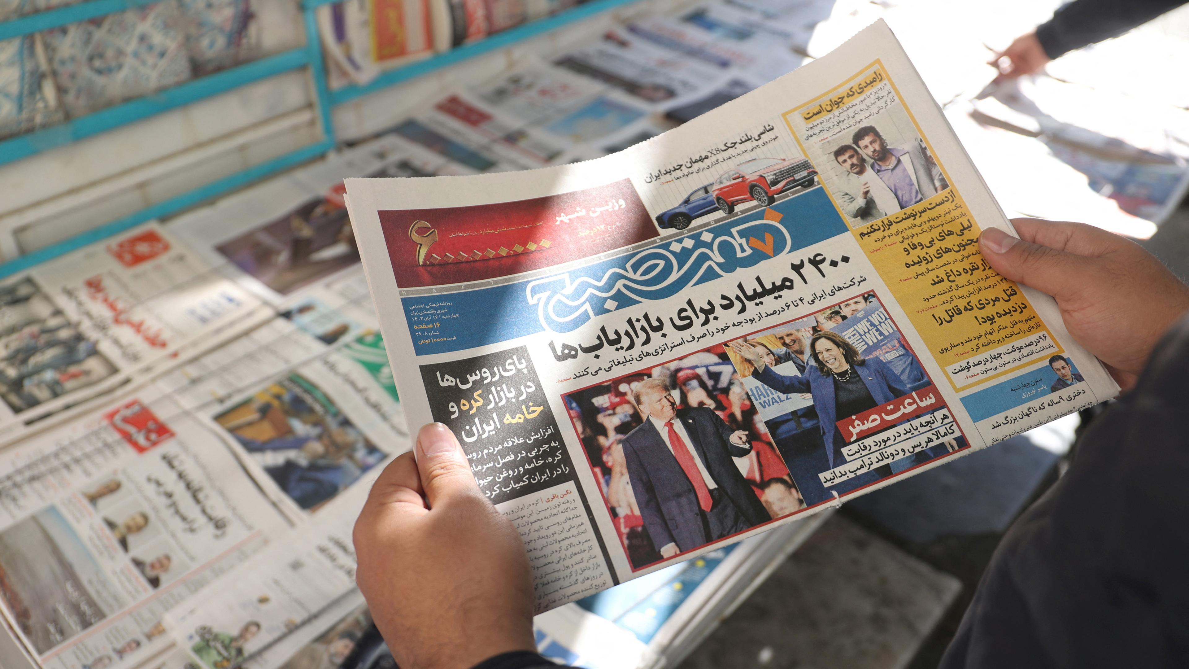 An Iranian man looks at a newspaper with a picture of Trump and Harris, in Tehran