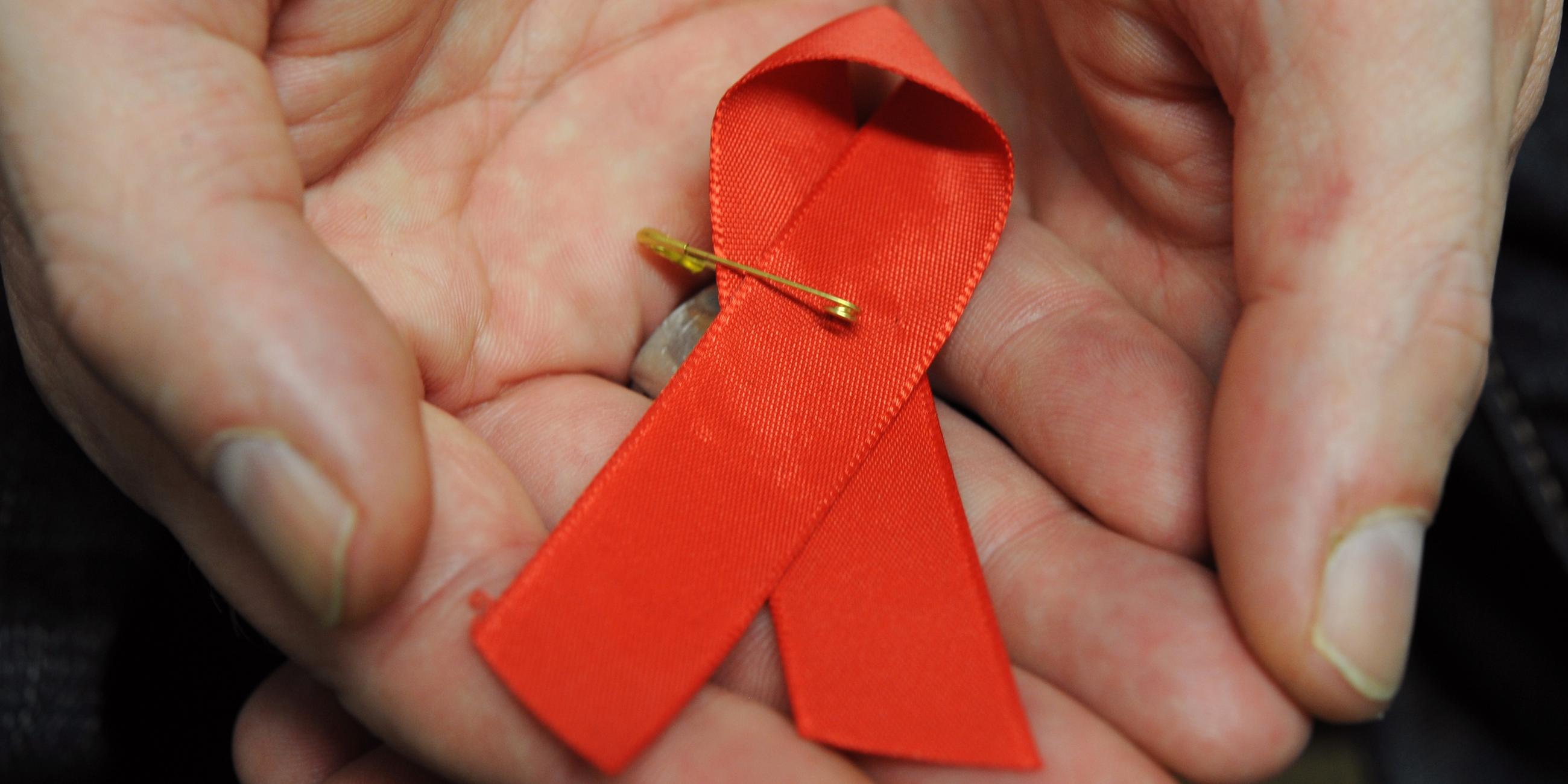 Hessen, Frankfurt/Main: Ein mit dem HI-Virus infizierter Mann hält eine rote Schleife als Symbol der Solidarität mit HIV-Positiven und Aids-Kranken.