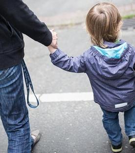 Eine Mutter hält ihren Sohn an der Hand und überquert die Straße.