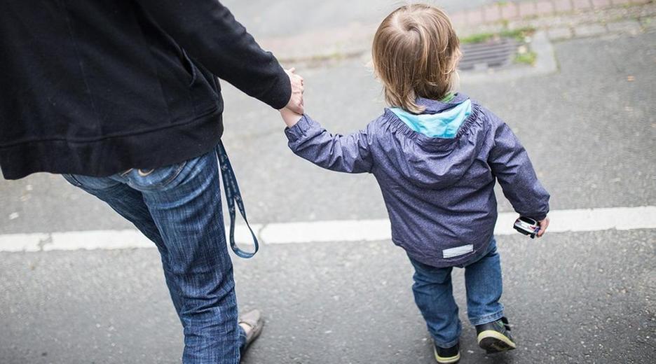 Eine Mutter hält ihren Sohn an der Hand und überquert die Straße.