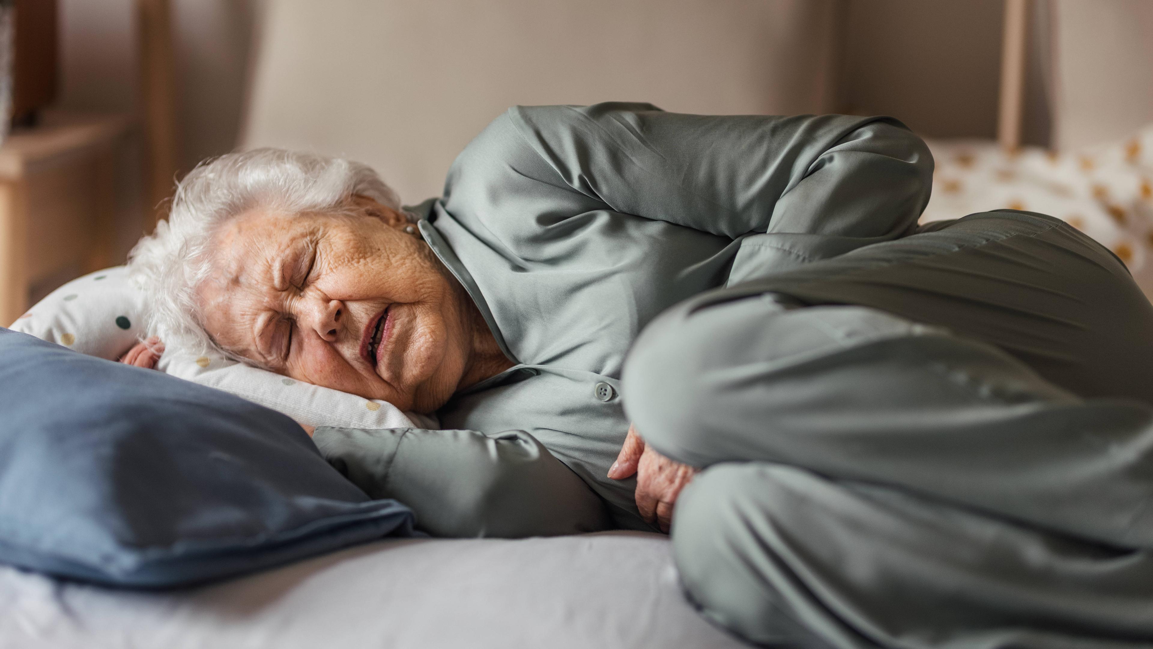 Eine ältere Frau liegt seitlich im Bett und versucht zu schlafen. Ihr Gesichtsaudruck deutet auf Schmerzen hin. 