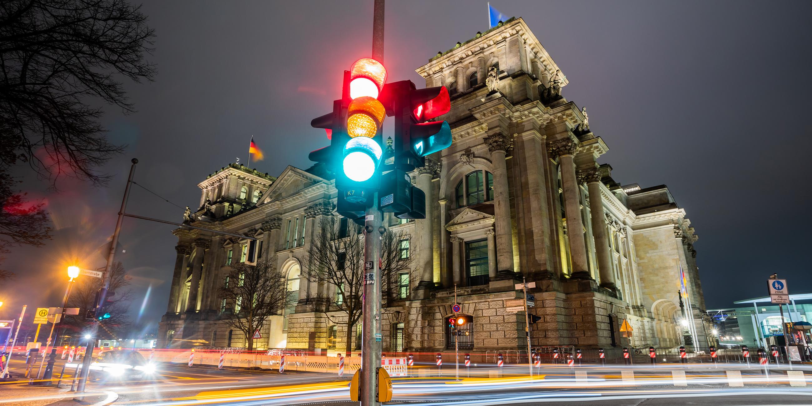 Eine Ampel leuchtet in einer Aufnahme mit Langzeitbelichtung am Morgen vor dem Reichstagsgebäude