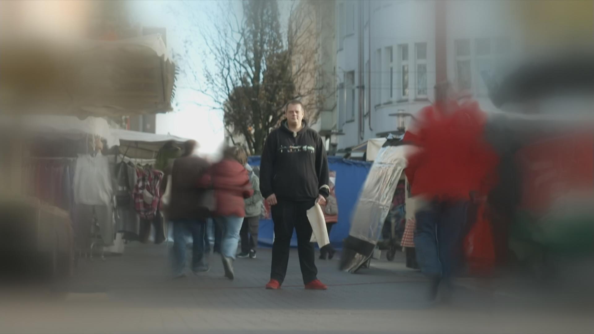 Ein Betroffener auf einem Marktplatz. Die Ränder des Bildes sind verschwommen.