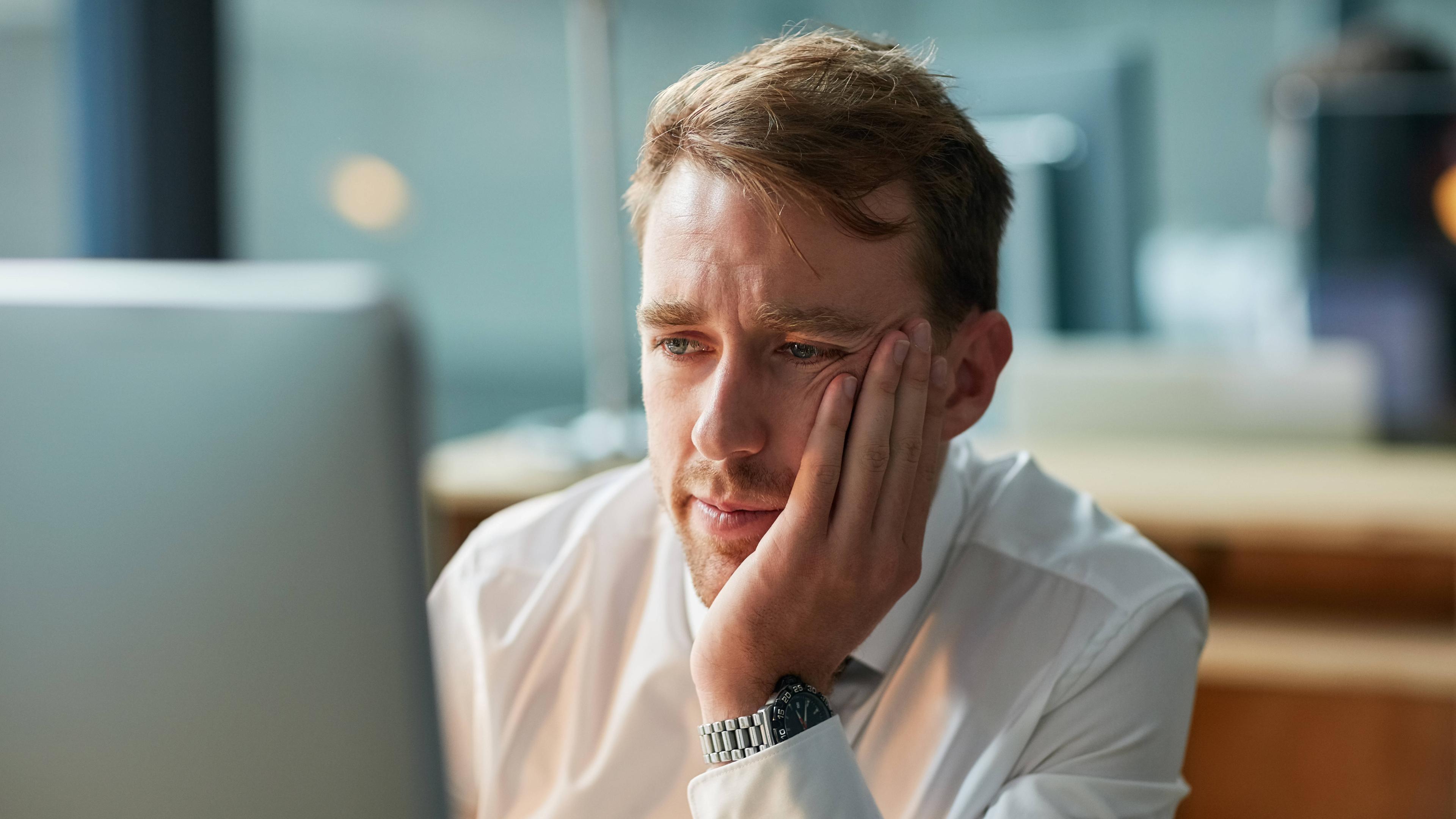 Ein Mann in einem Büro sitzt vor einem Computer und schaut auf den Bildschirm.