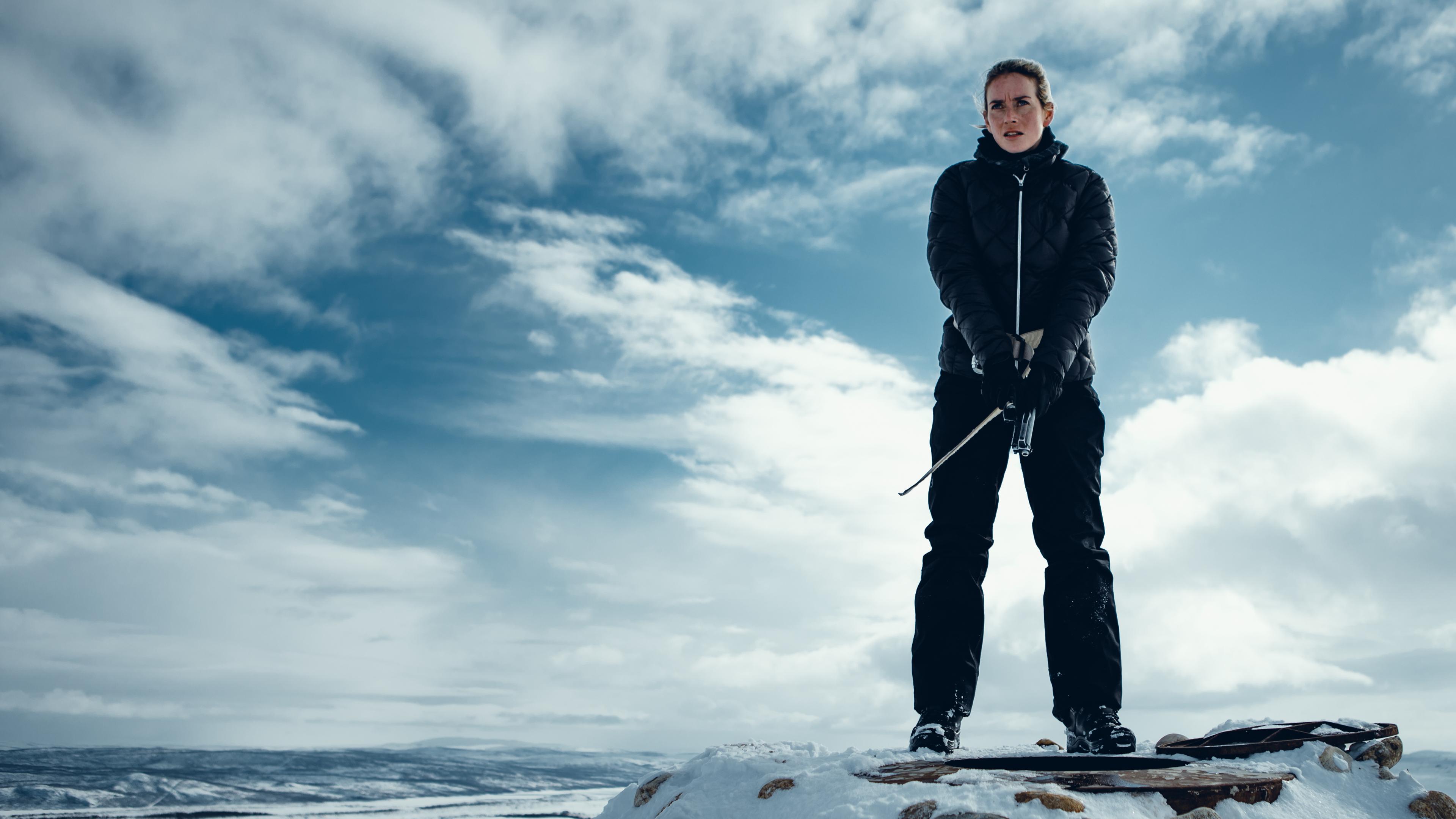 "Arctic Circle - Der unsichtbare Tod (10)": Nina Kautsalo (Iina Kuustonen) steht auf einem schneebedeckten Berg. Über ihr am Himmel sieht man Wolkenformationen.