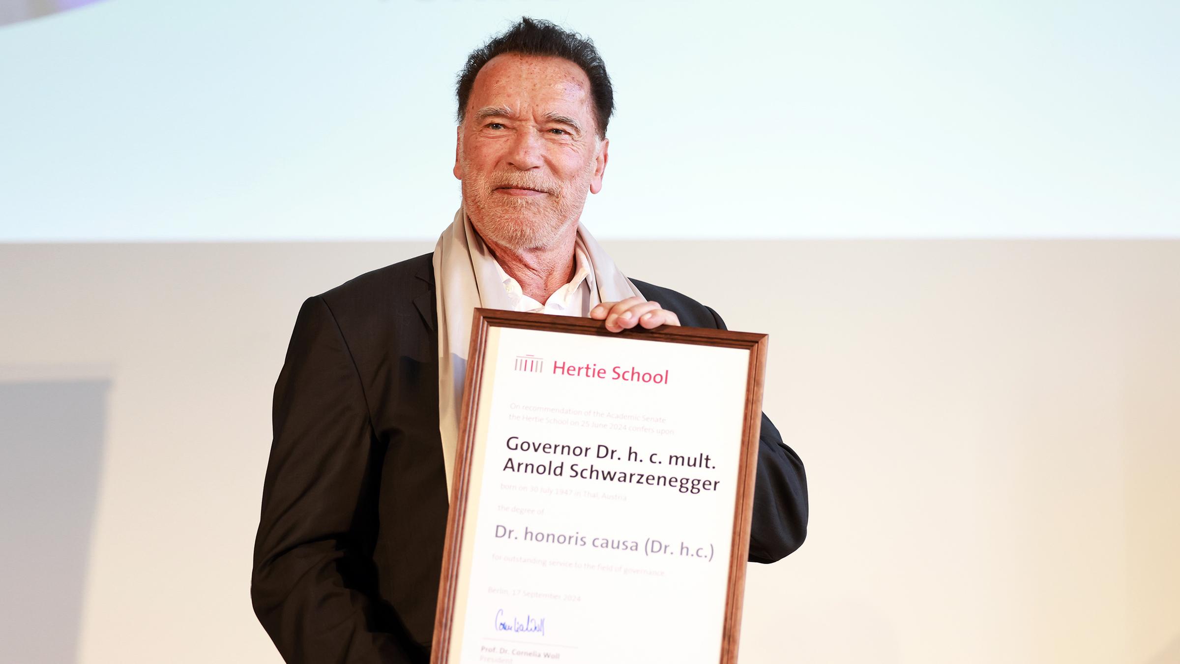 Arnold Schwarzenegger hät seine Ehrendoktor-Urkunde in der Hand.