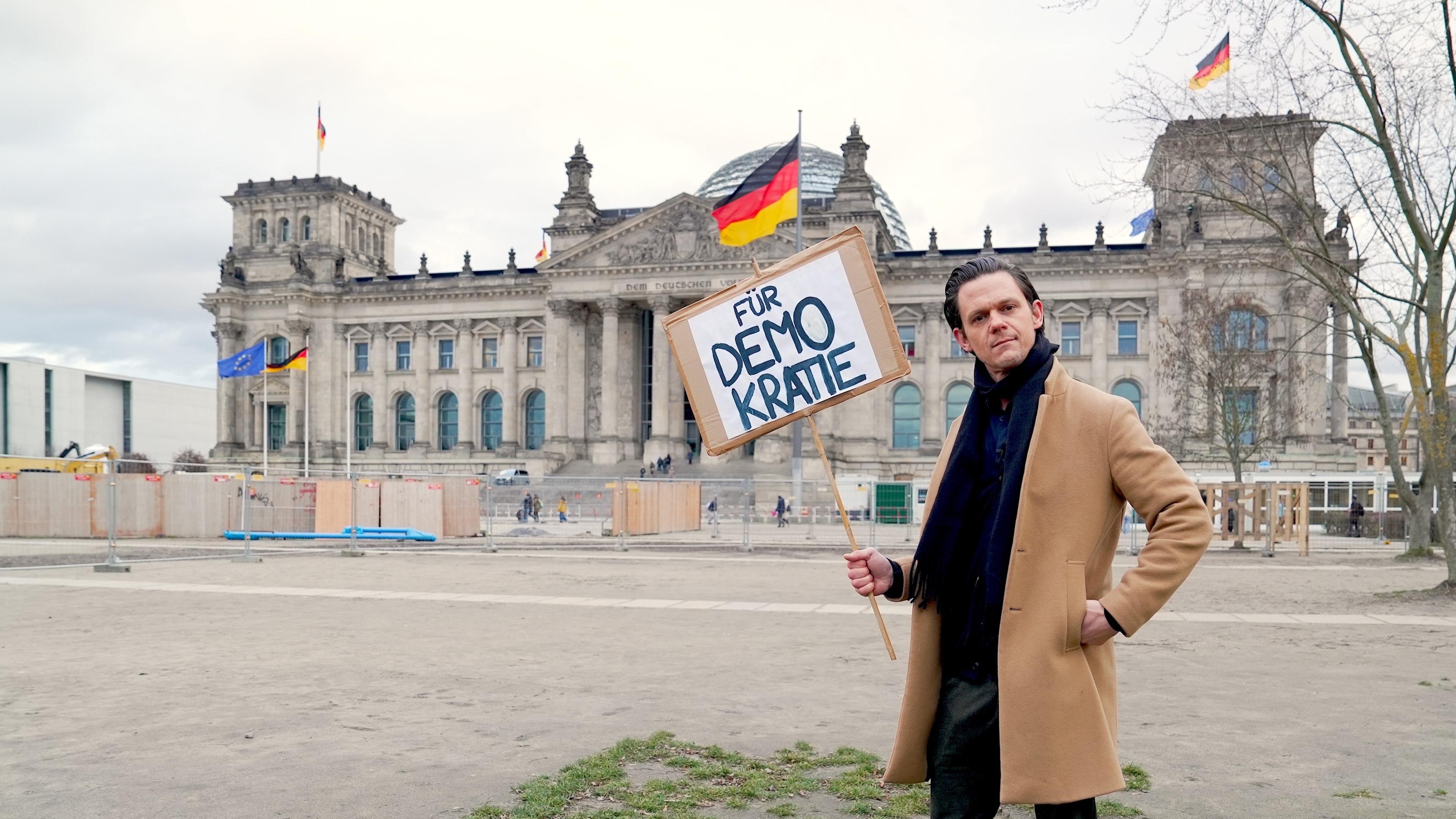 aspekte-Moderator Jo Schück mit Demokratieschild vor Reichstag