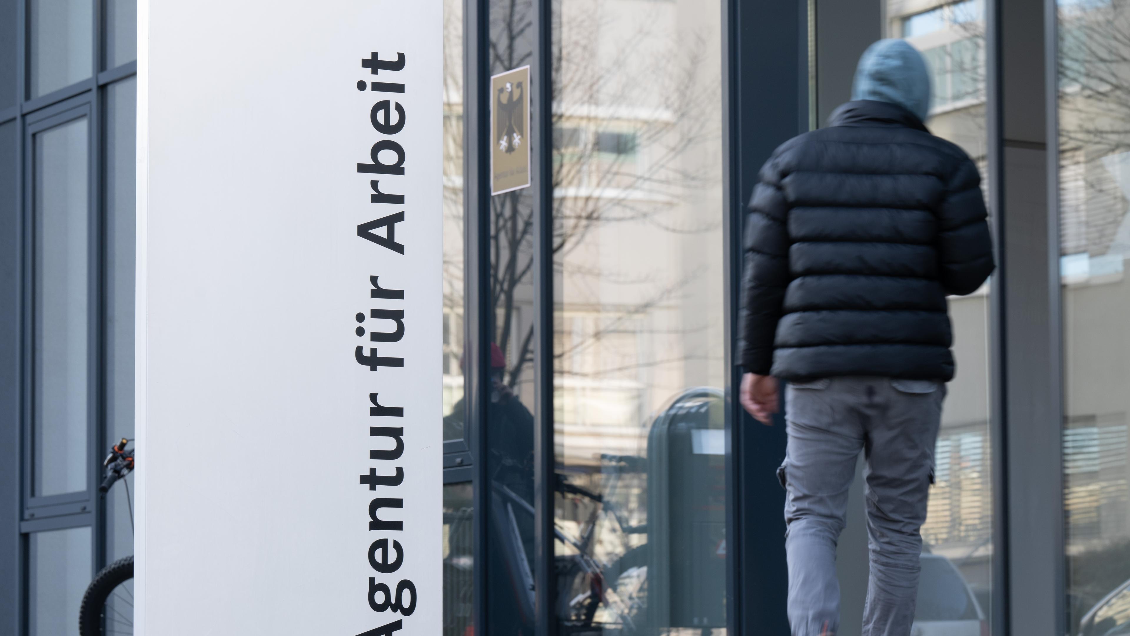 Ein Mann läuft neben einem Schild für die Agentur für Arbeit