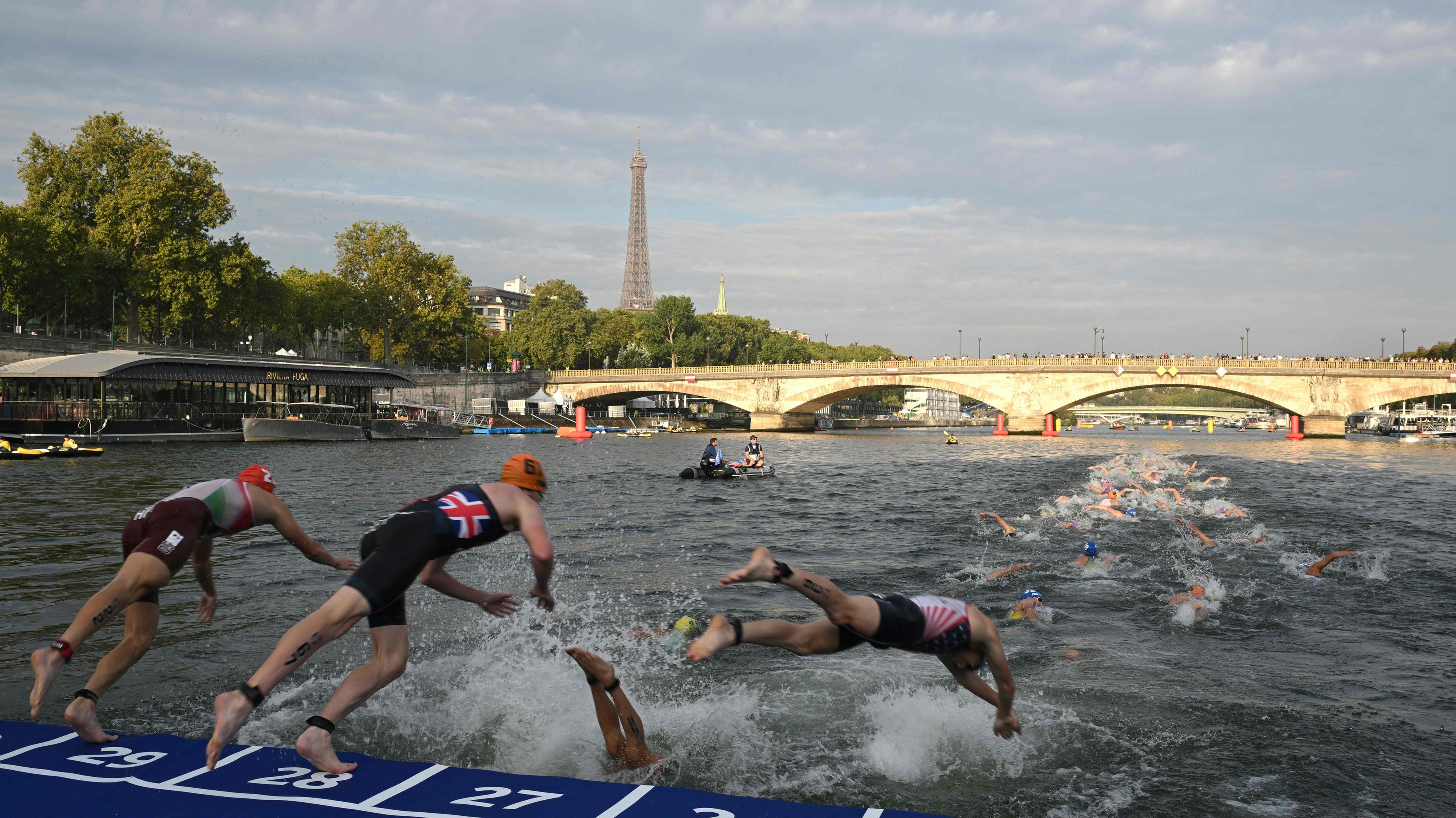 Triathlon-Athleten tauchen während des Testevents der Olympischen Triathlon-Weltmeisterschaft der Männer 2023 in Paris in die Seine ein, mit dem Eiffelturm im Hintergrund.