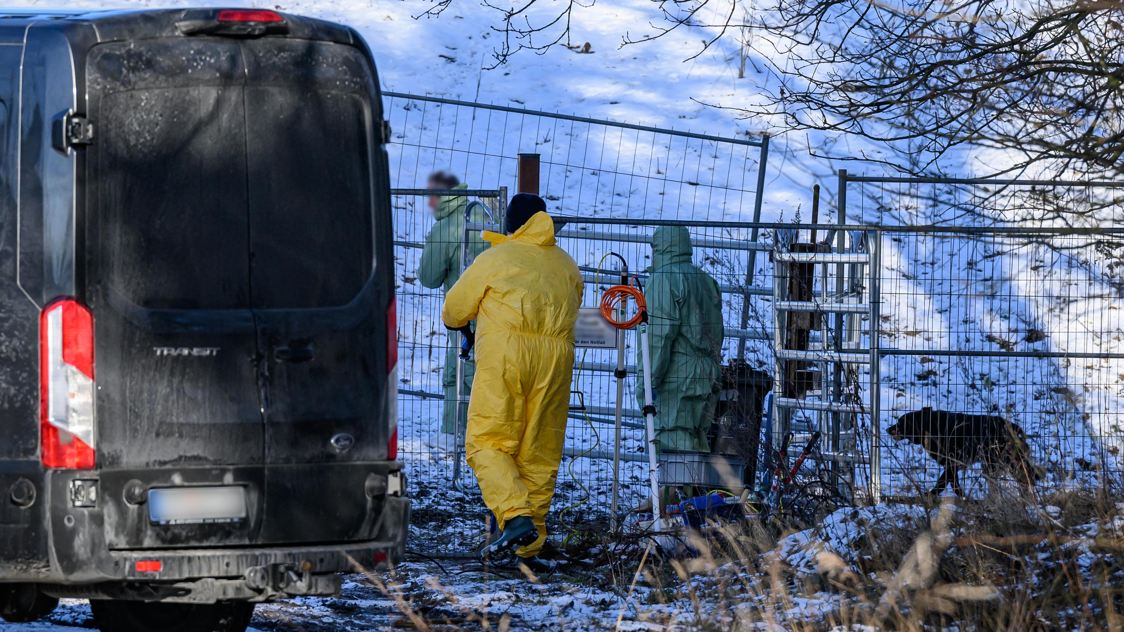 Brandenburg, Schöneiche: Personen in Schutzkleidung gehen über eine Weide, während Feuerwehr und Polizei das Gelände weiträumig abgesperrt haben.