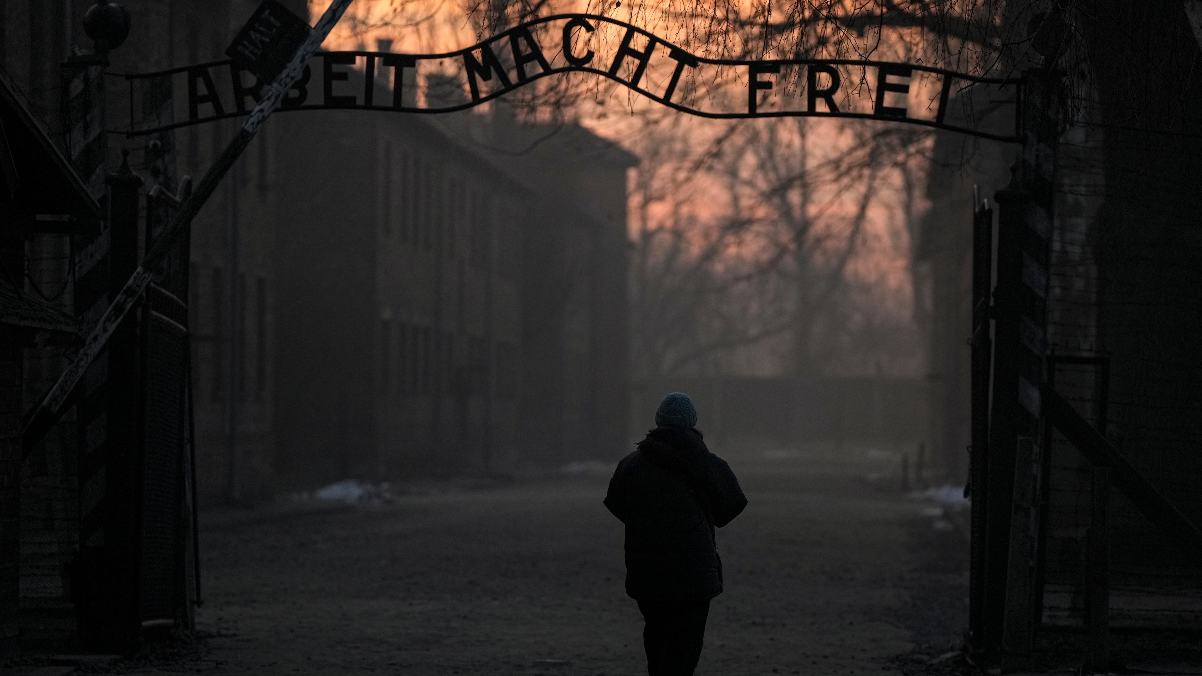 Eine Person geht zum Tor des ehemaligen deutschen Konzentrations- und Vernichtungslagers Auschwitz-Birkenau mit dem Schriftzug "Arbeit macht frei".