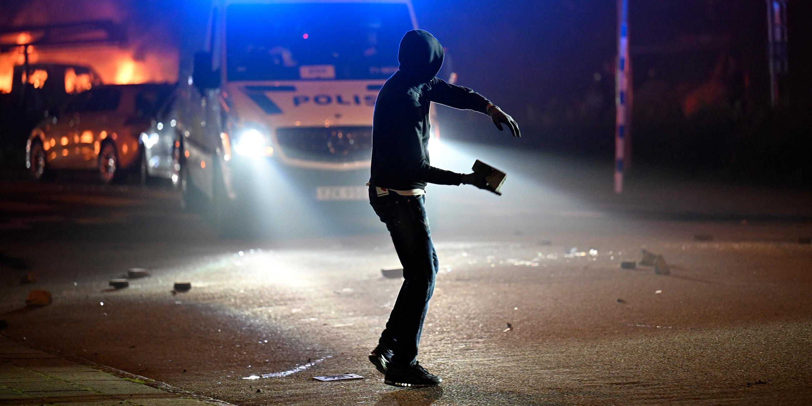 Ein Demonstrant wirft einen Stein auf ein Polizeifahrzeug