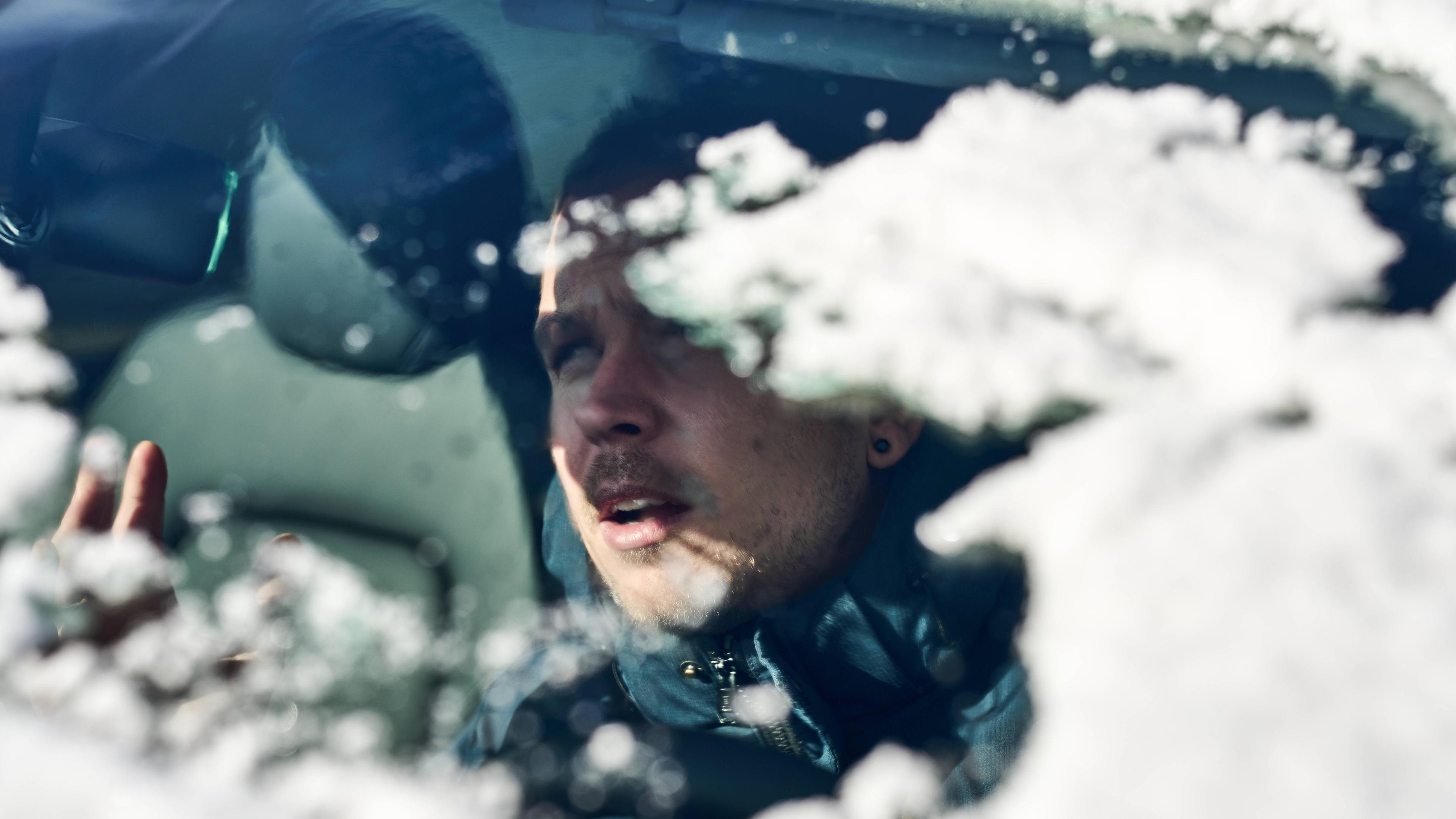 Ein Mann sitzt im Auto und blickt durch die verschneite Windschutzscheibe.