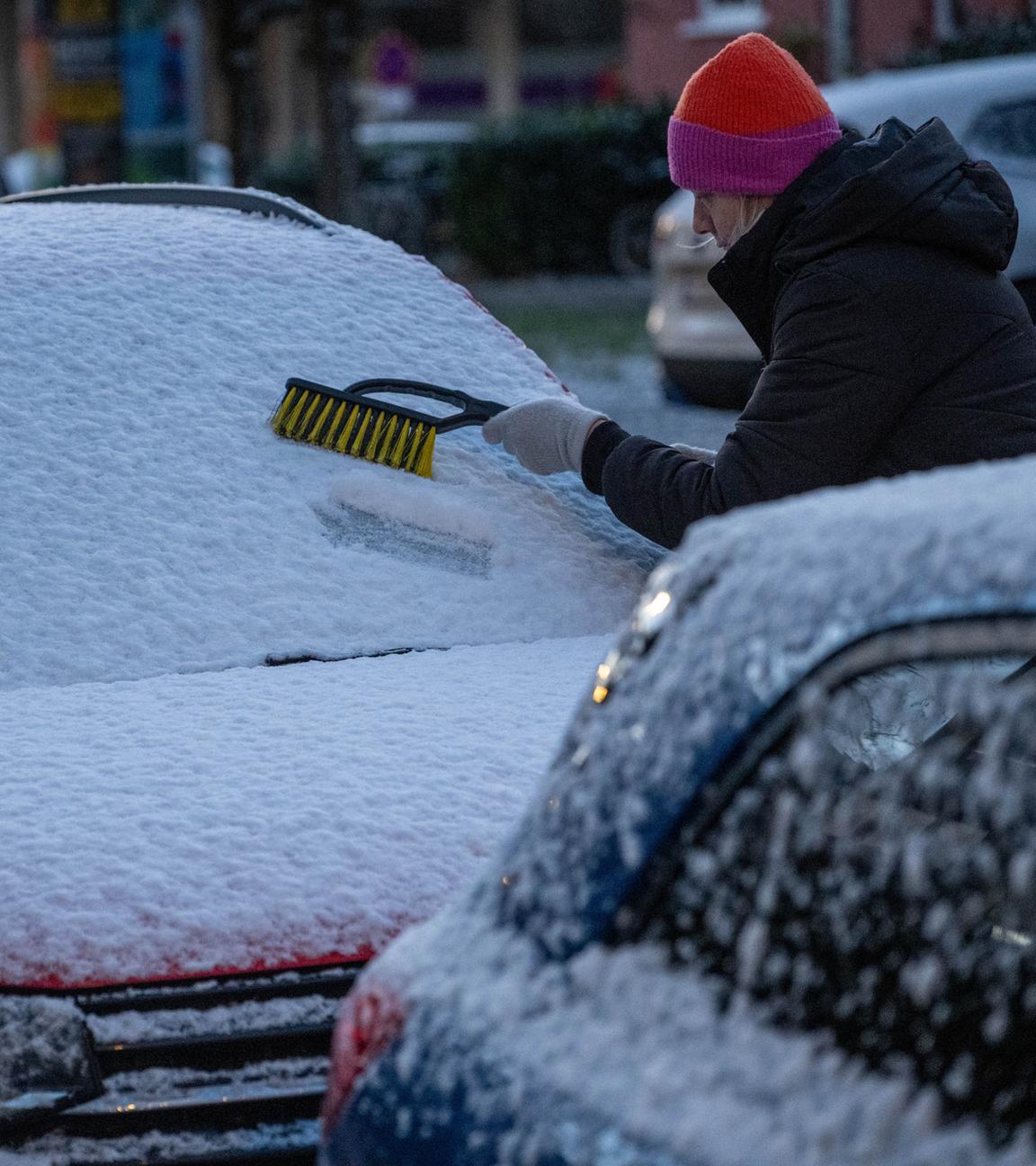 Eine Frau befreit am frühen Morgen ein Auto von Schnee und Eis.