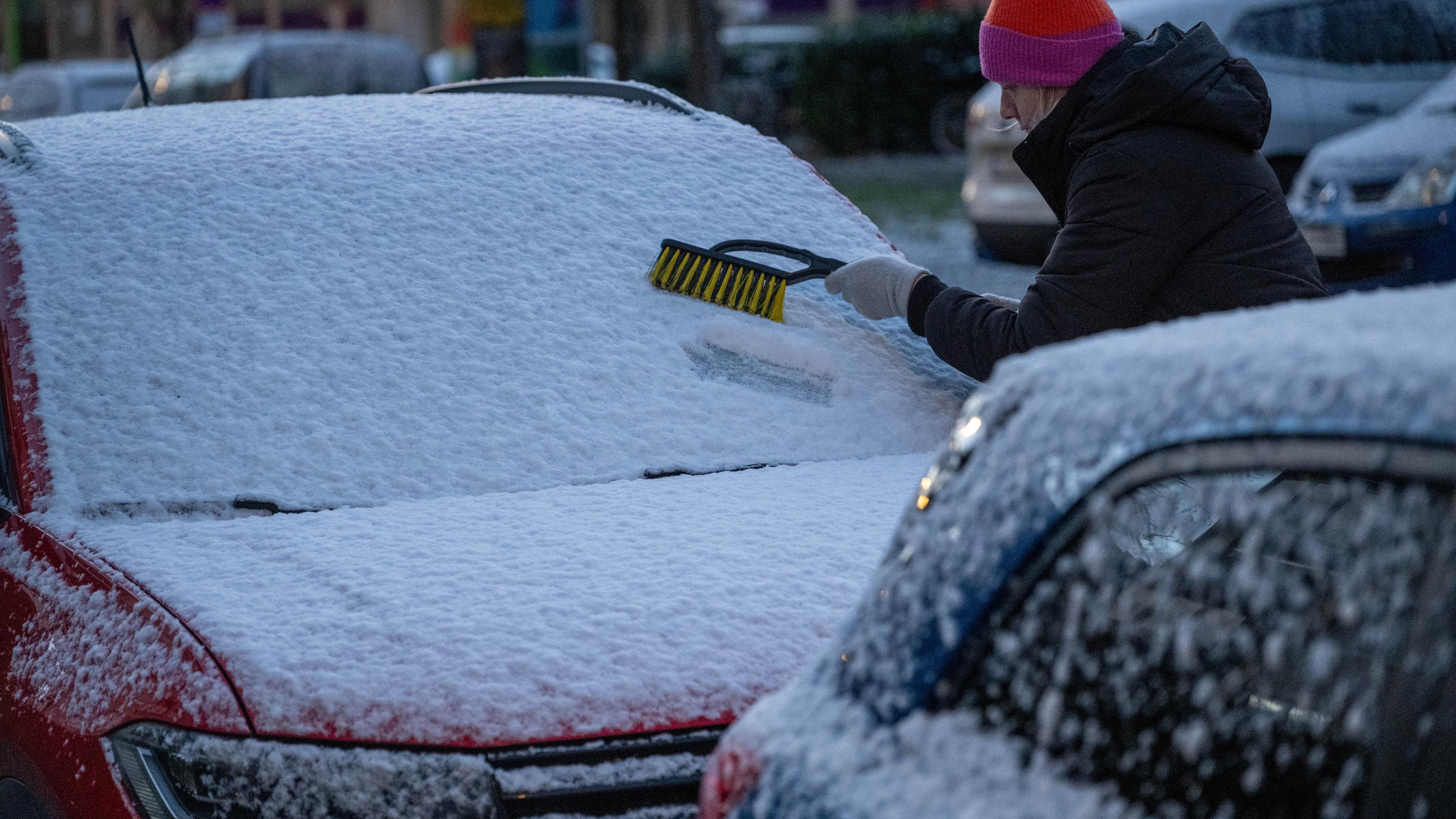 Eine Frau befreit am frühen Morgen ein Auto von Schnee und Eis.