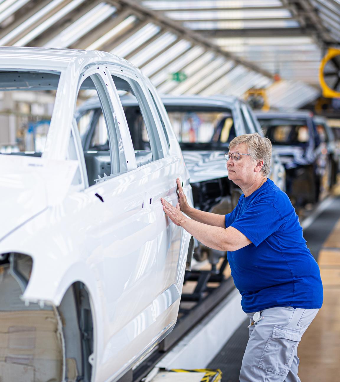 Niedersachsen, Wolfsburg: Eine Mitarbeiterin überprüft im Lichttunnel einer Autofabrik den Lack von Karosserien.