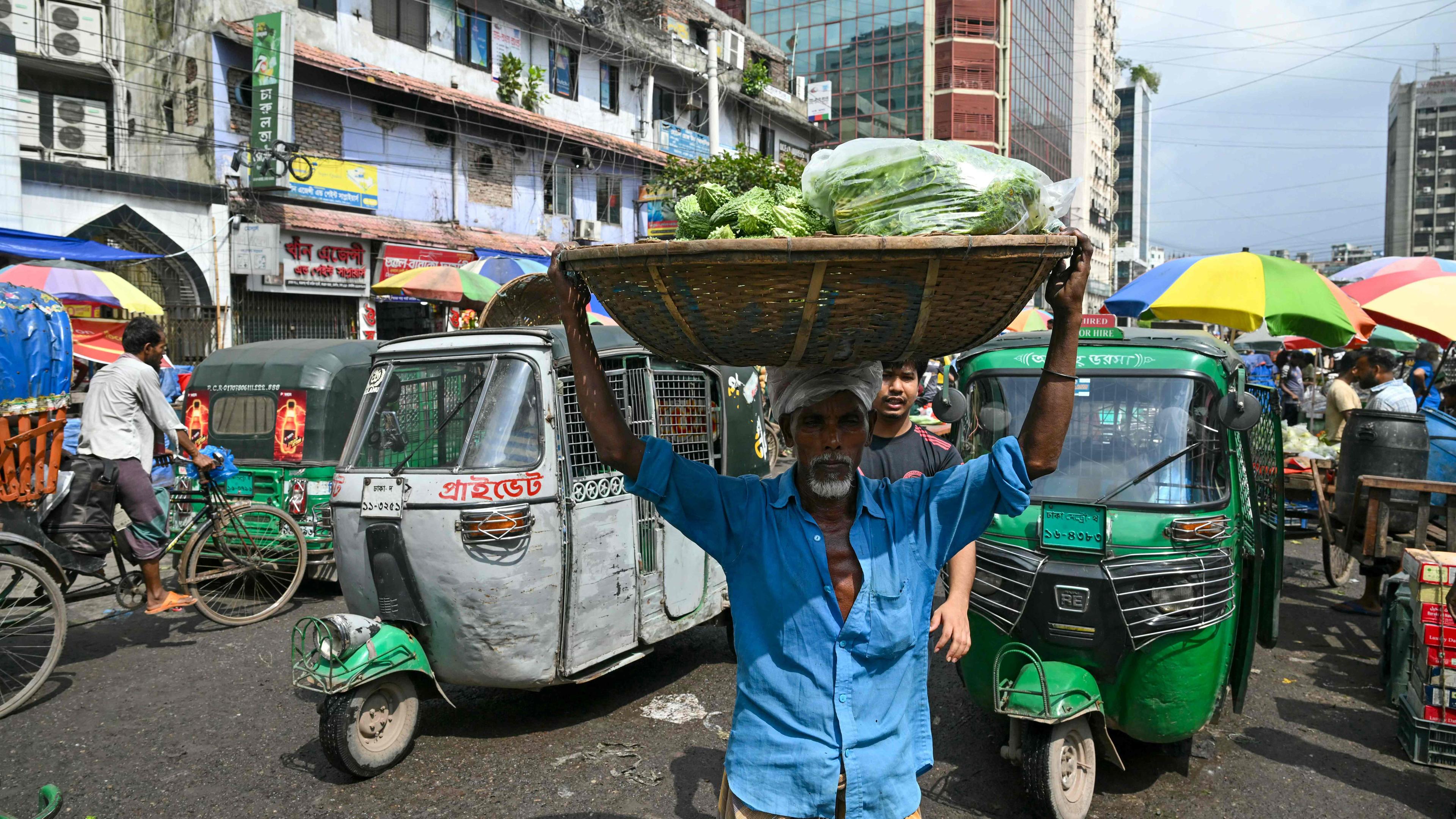 Ein Mann trägt einen Korb voller Gemüse in einer Straße in Dhaka, Bangladesch.