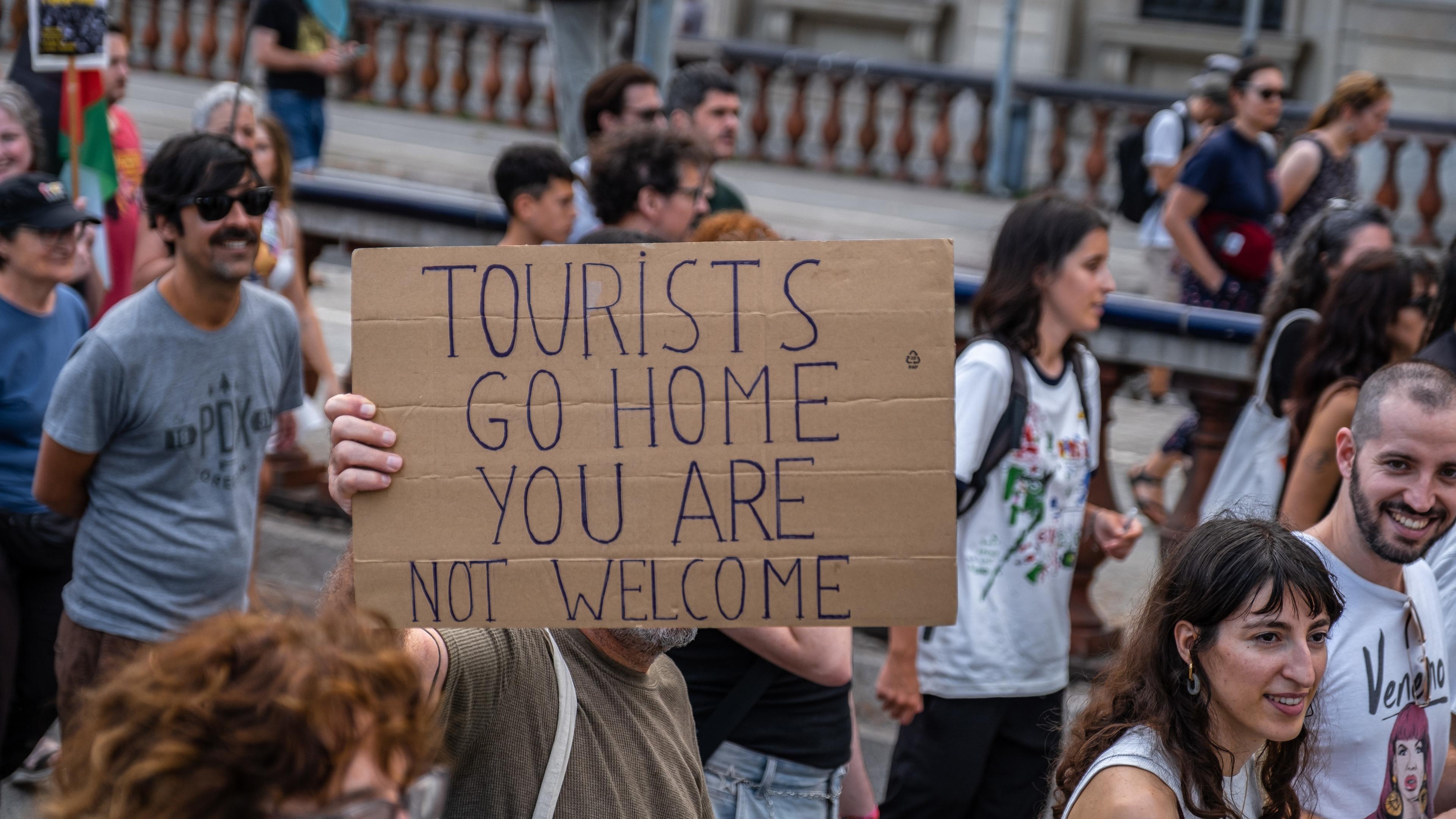 Eine Demonstration gegen Massentourismus in Barcelona. Auf einem Schild steht in Englisch geschrieben: "Touristen, geht nach Hause. Ihr seid nicht willkommen."