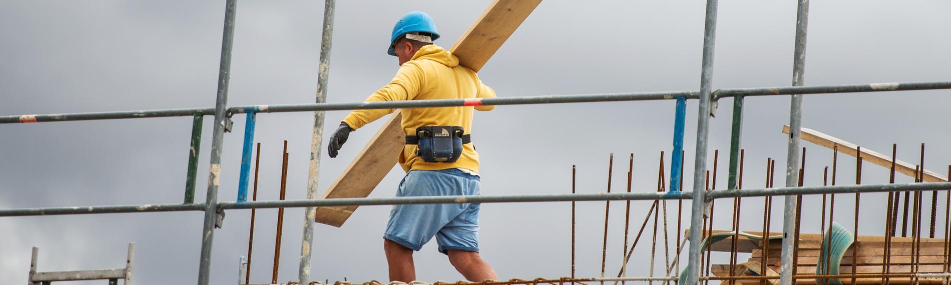 Ein bauarbeiter trägt auf einer Baustelle auf einem Hausdach ein Brett, aufgenommen am 08.07.2019