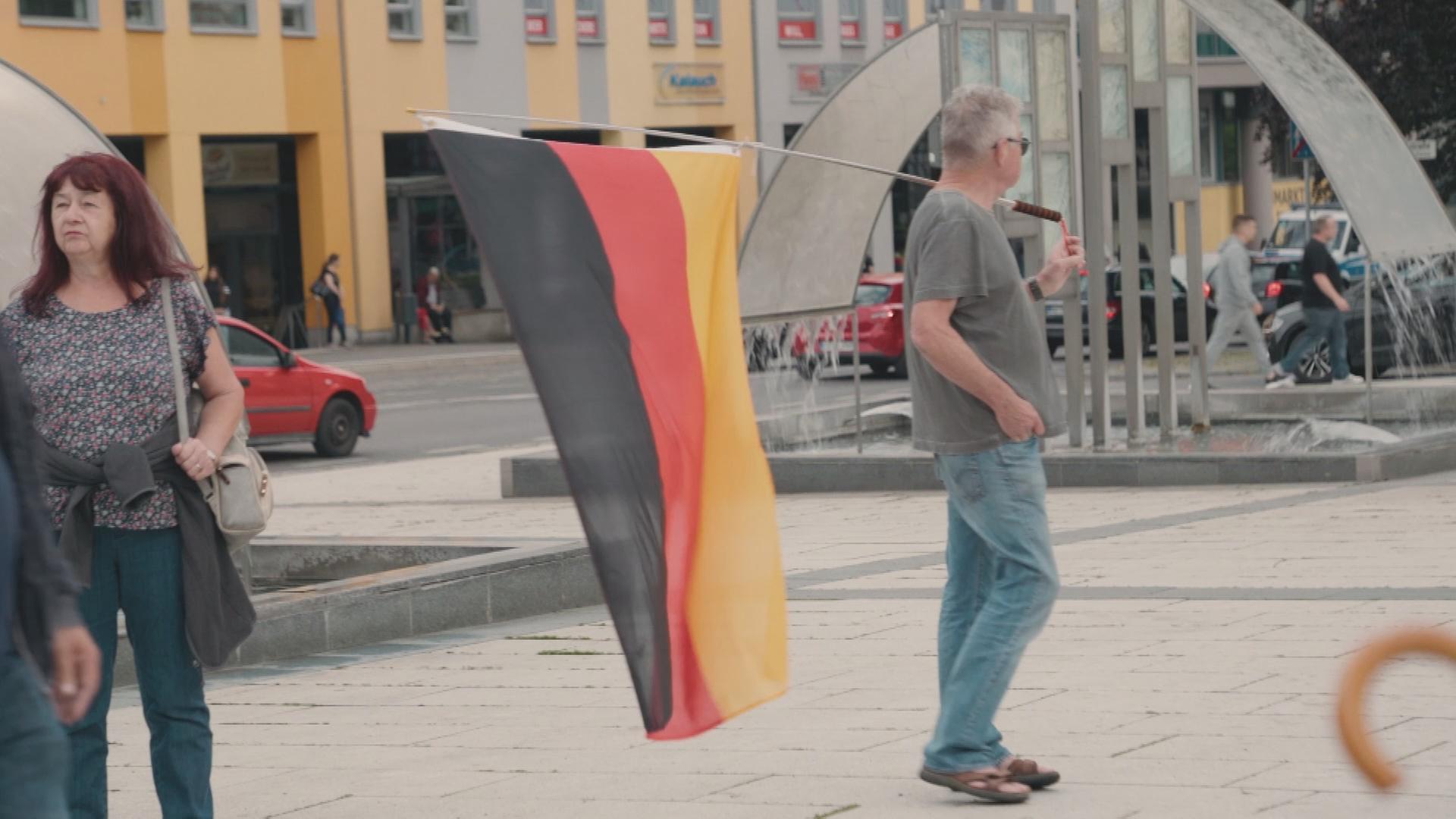 Ein Mann trägt in Bautzen eine Deutschland-Fahne über der Schulter. Er blickt zur Seite.