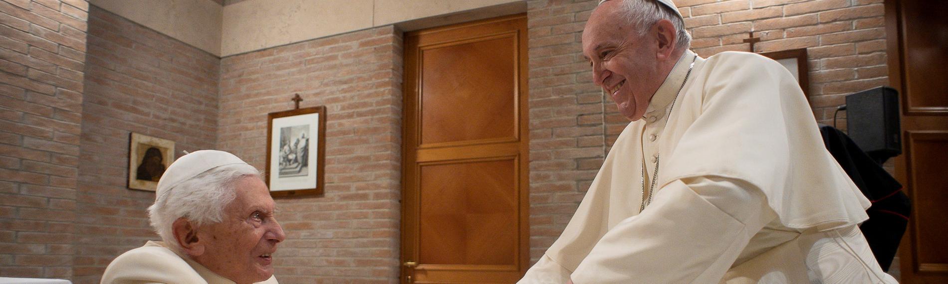 Papst Benedikt XVI. und Papst Franziskus reichen sich die Hände im Vatikan.