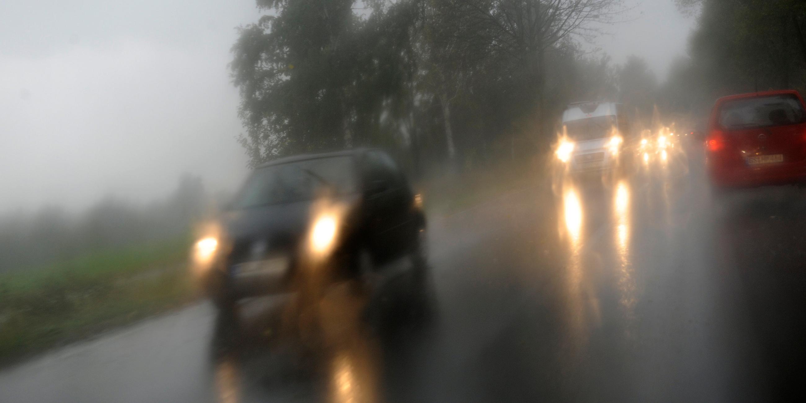 Blick durch die Windschutzscheibe auf schemenhafte Fahrzeuge auf einer Straße während es regnet.