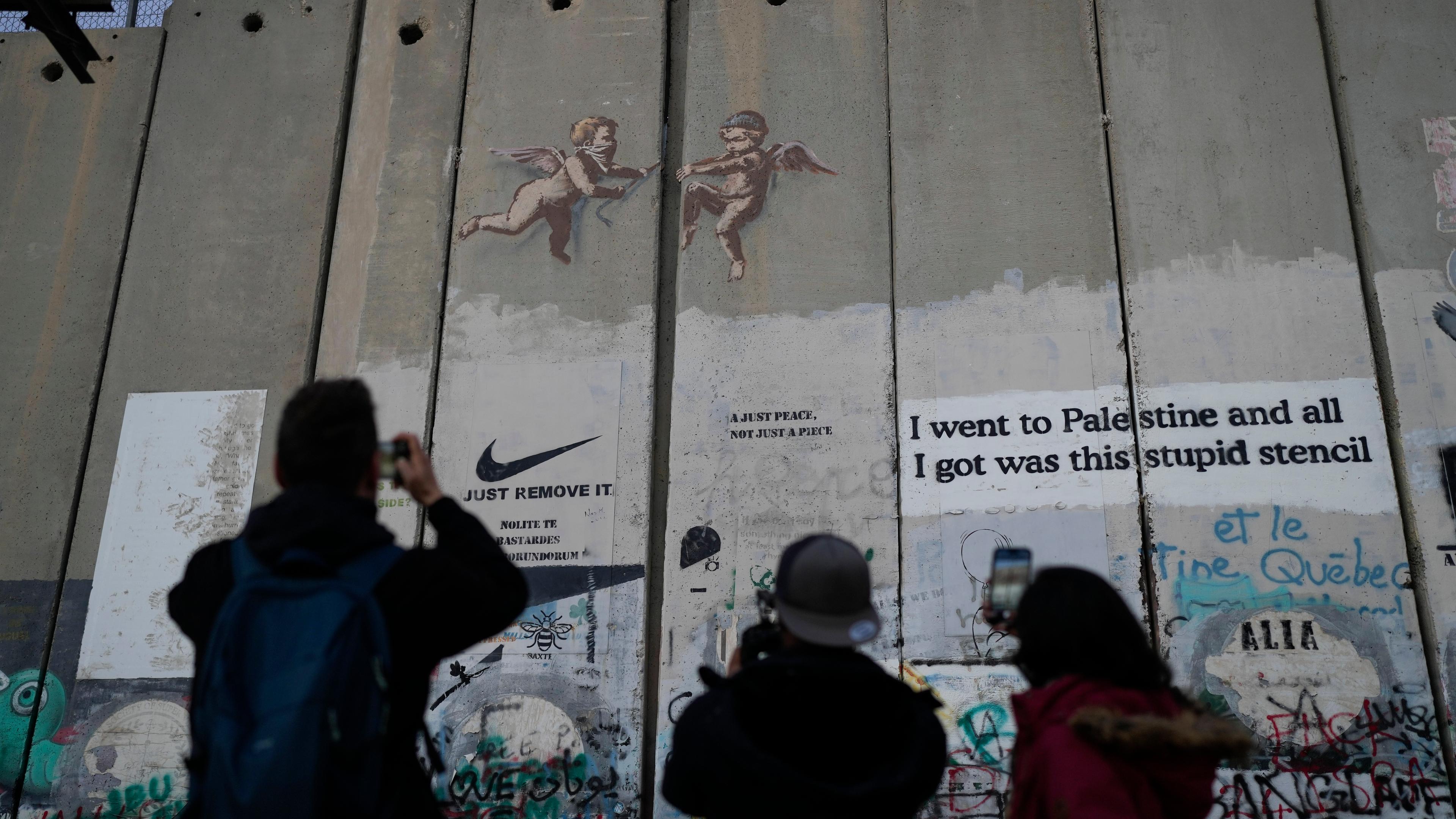 Touristen fotografieren an Heiligabend ein Banksy-Graffiti auf der Trennmauer in Bethlehem im Westjordanland