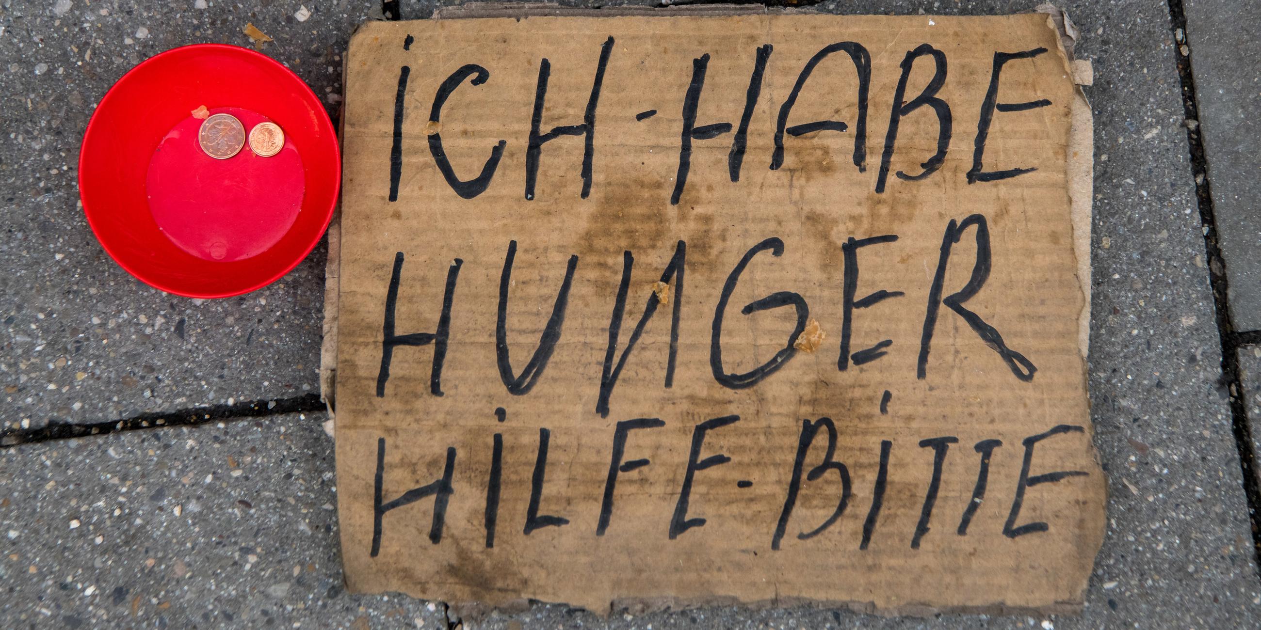 Eine rote Schale mit ein paar Cent-Geldstücken und ein Pappschild mit der Aufschrift "ich habe Hunger - Hilfe bitte"