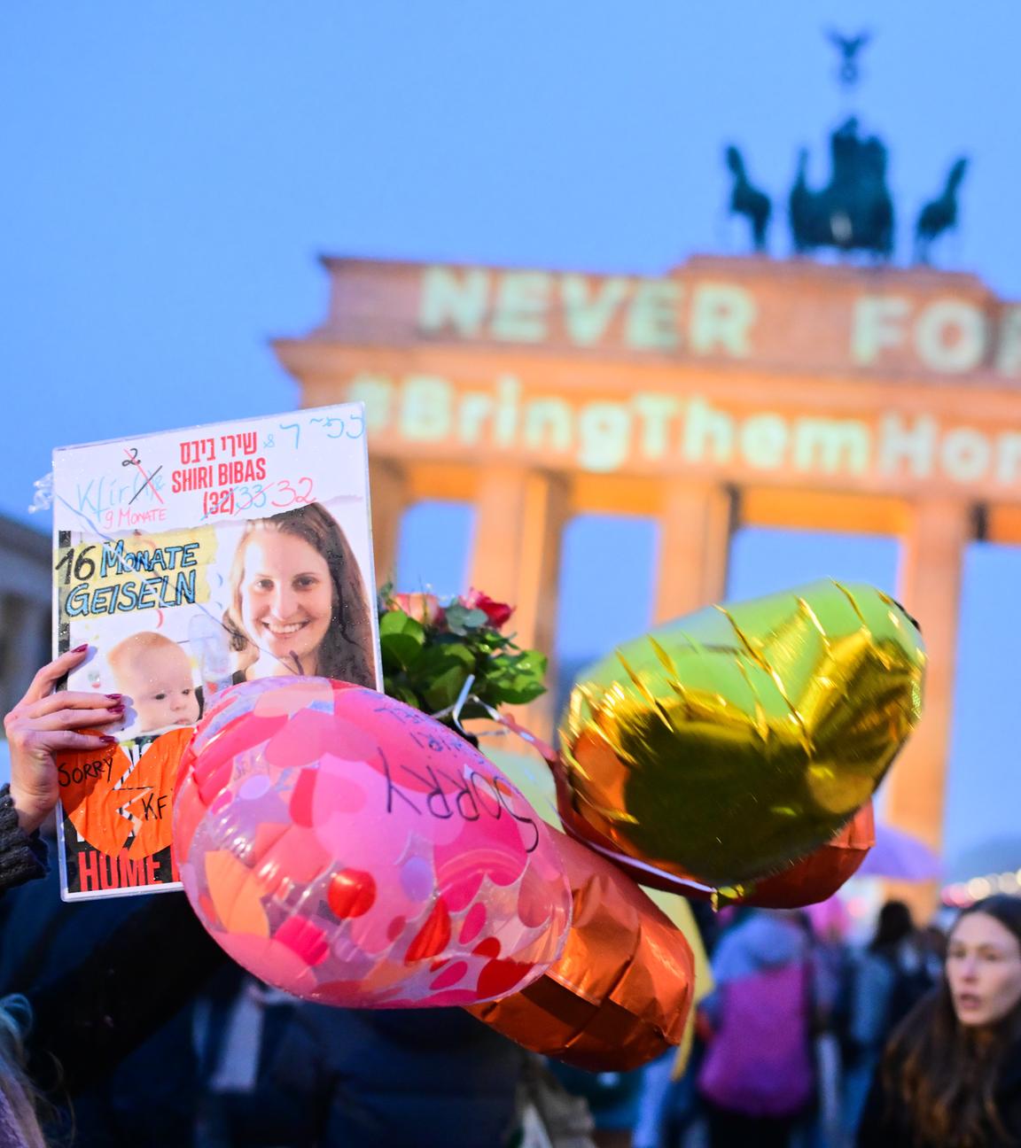 Berlin: Eine Frau hält ein Bild von Shirin Bibas vor dem Brandenburger Tor hoch, auf dem die Schriftzüge "Never forget" und "#BringThemHomeNow" projiziert sind.