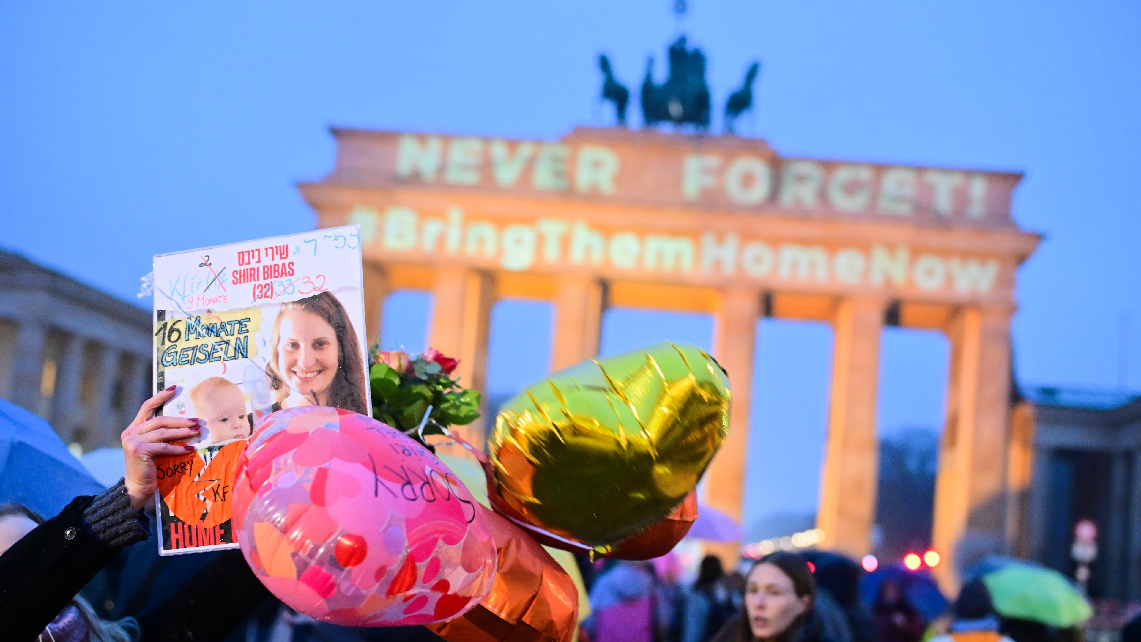 Berlin: Eine Frau hält ein Bild von Shirin Bibas vor dem Brandenburger Tor hoch, auf dem die Schriftzüge "Never forget" und "#BringThemHomeNow" projiziert sind.