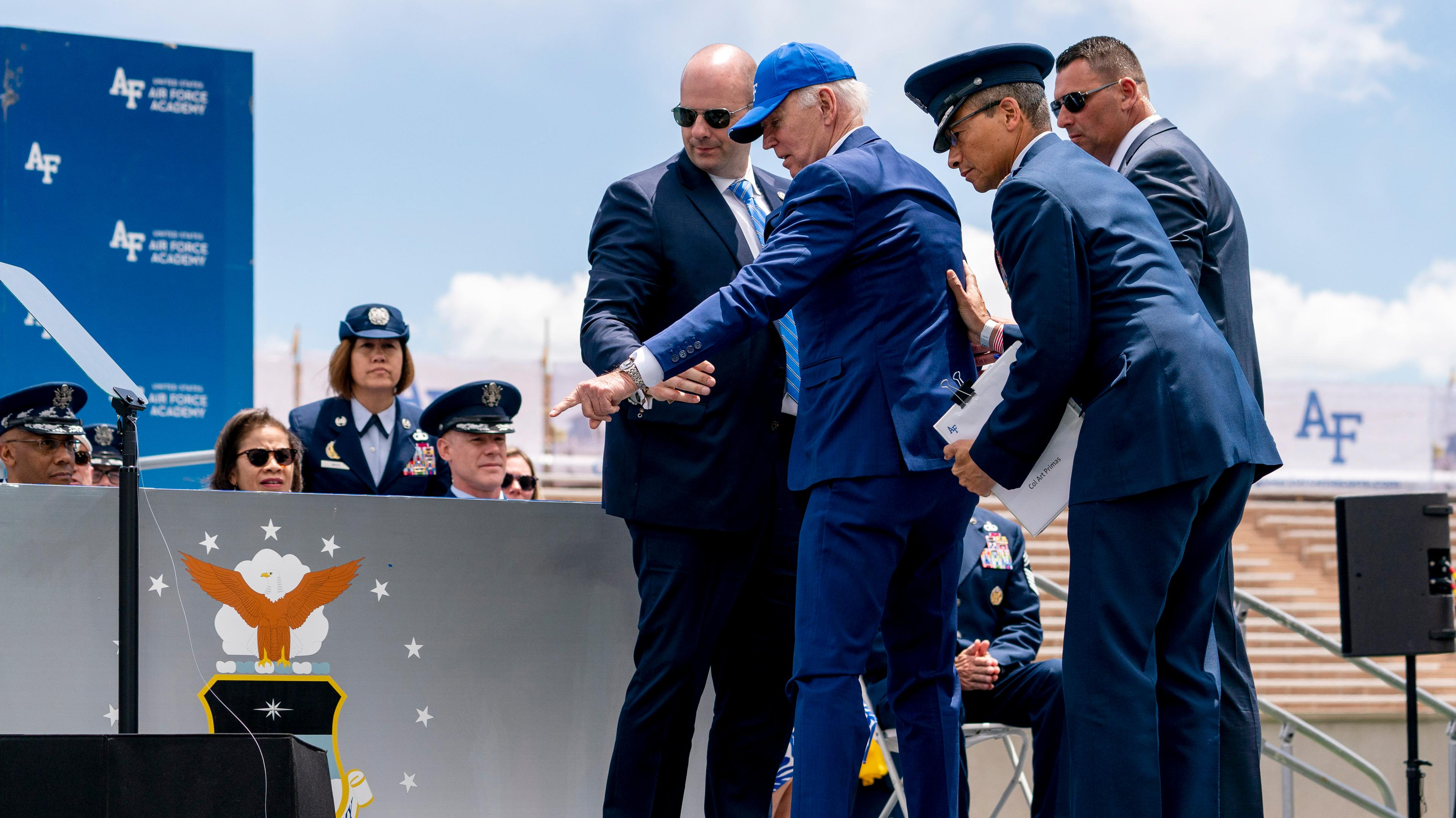 US-Präsident Biden zeigt nach seinem Sturz bei einer Absolventenfeier der Air Force Academy auf den Sandsack, über den er gestolpert ist