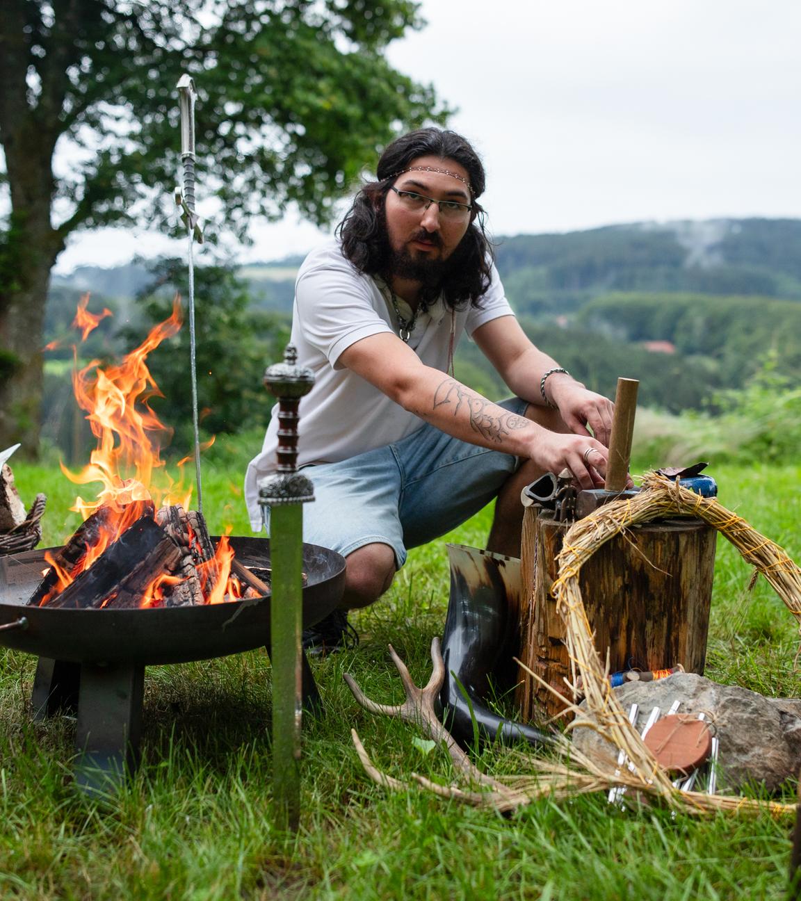 Junger Mann am Lagerfeuer mit Accecoires, die typisch für das Heidentum sind.