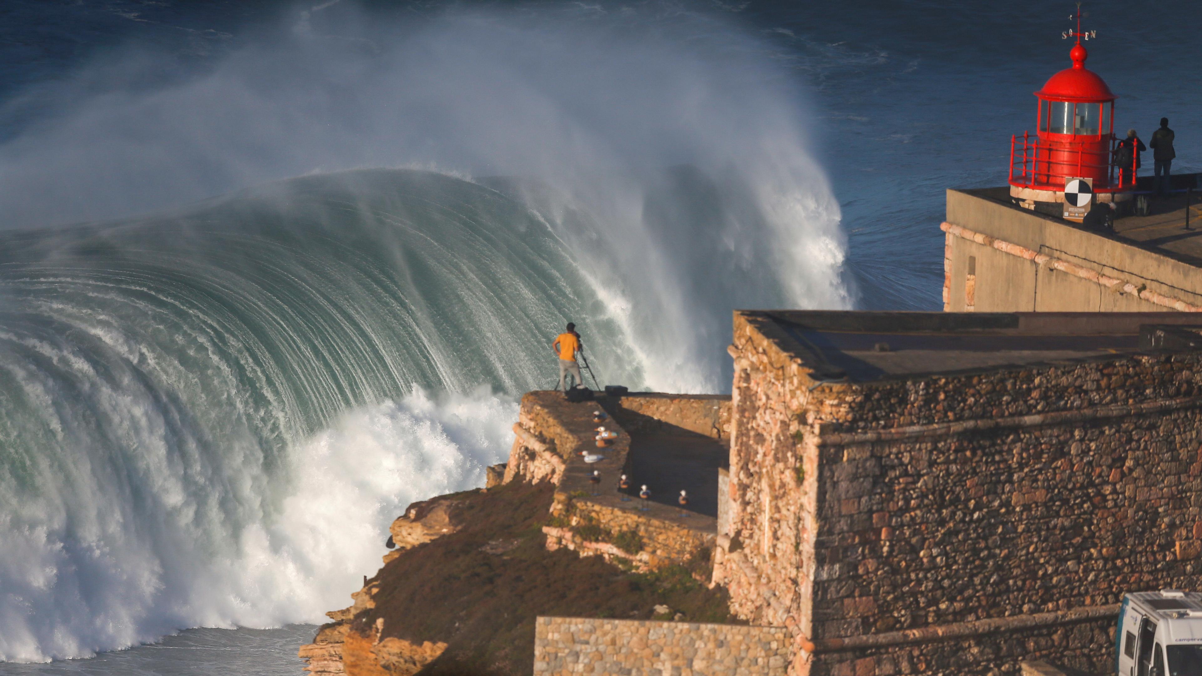 Auf dem Foto sieht man eine Burg, oder eine Mauer, die direkt am Meer steht. Am Rande dieser Mauer steht ein Fotograf, der das Meer fotografiert. Das Hauptaugenmerk bei dem Foto liegt allerdings auf die riesige Welle auf dem Meer, die gerade in sich zusammenbricht. 