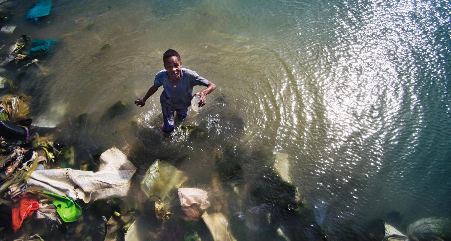 Ein Junge steht im Wasser voller Platikmüll