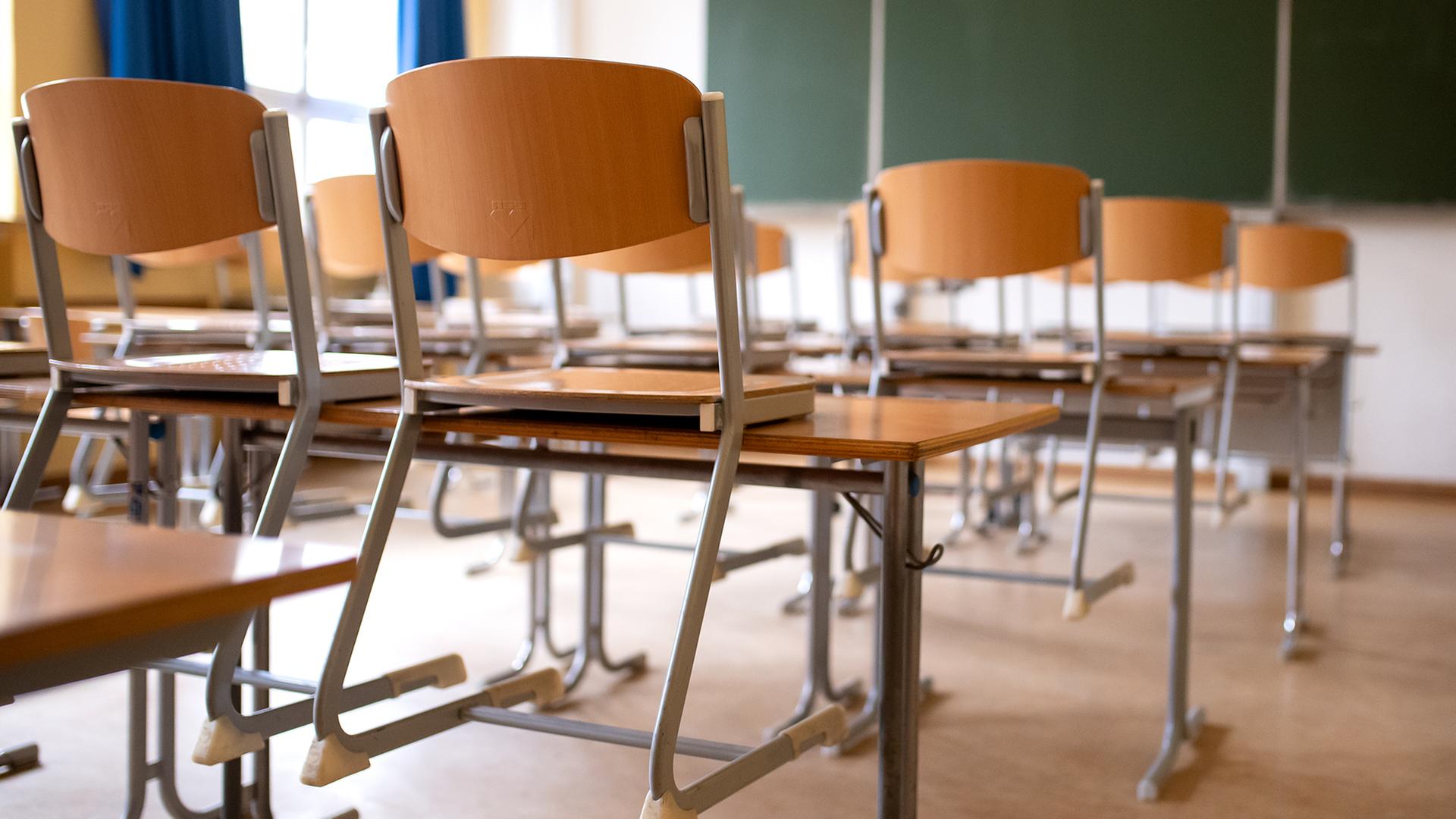 Ein leeres Klassenzimmer. Die Stühle sind auf die Tische gestellt. Im Hintergrund eine grüne Tafel.