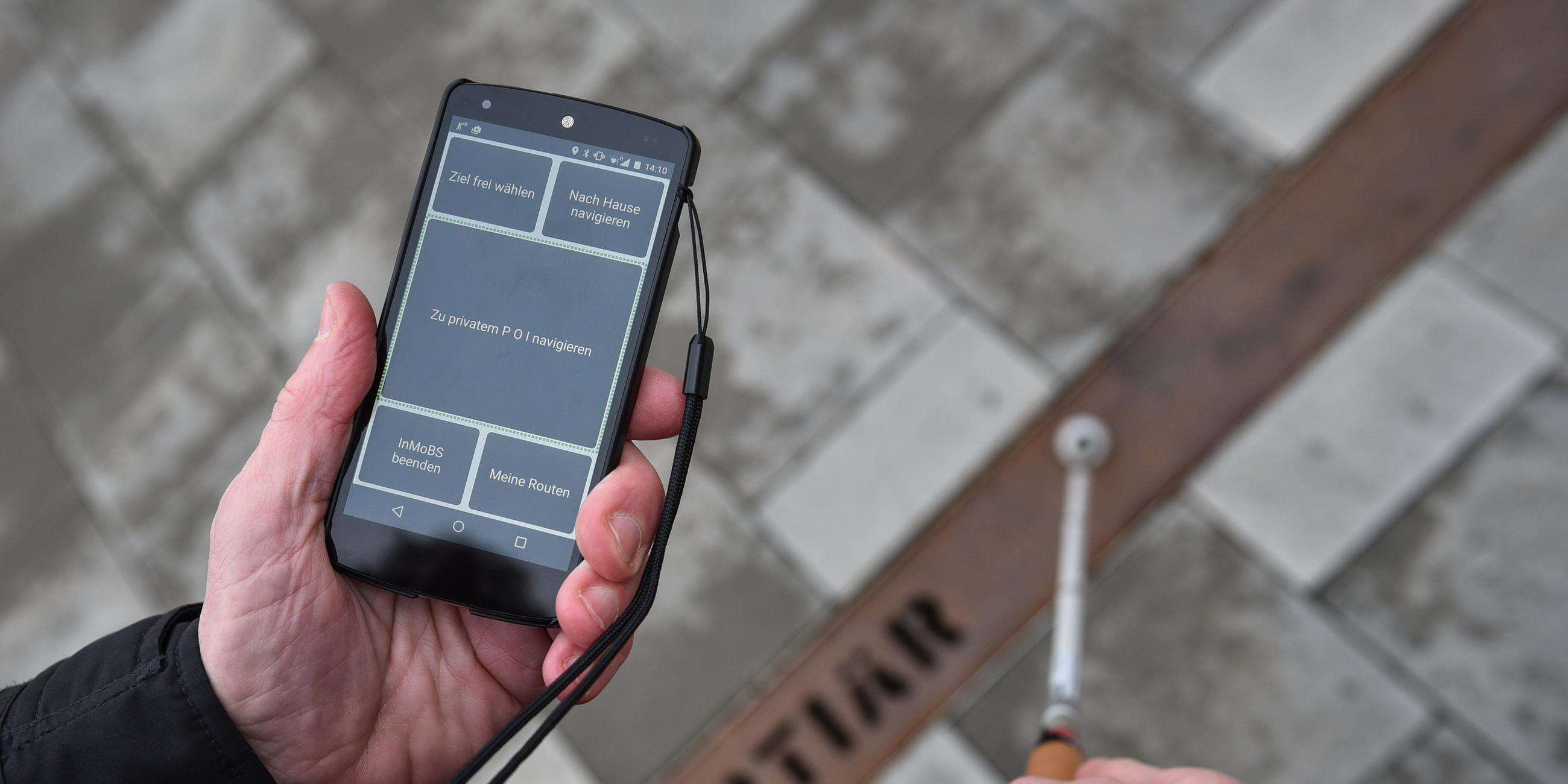 Mann hält Handy mit Verkehrsapp für Blinde und Blindenstock in Hand